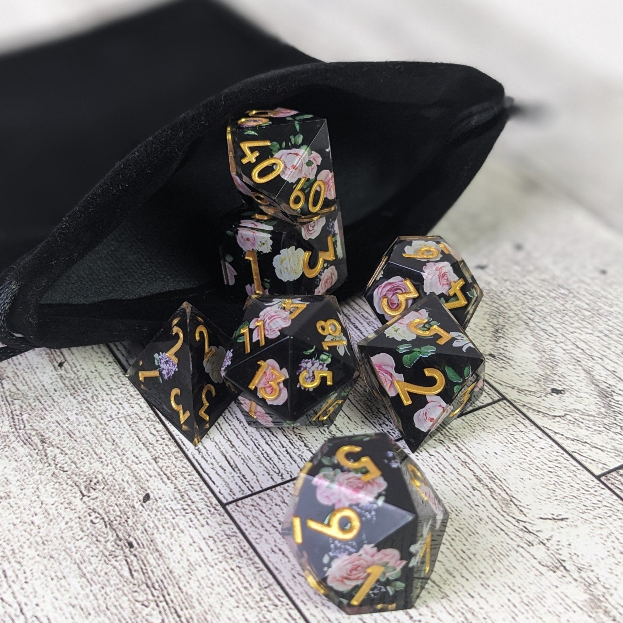 Set of black dice with floral designs and gold numbers on a wooden surface.