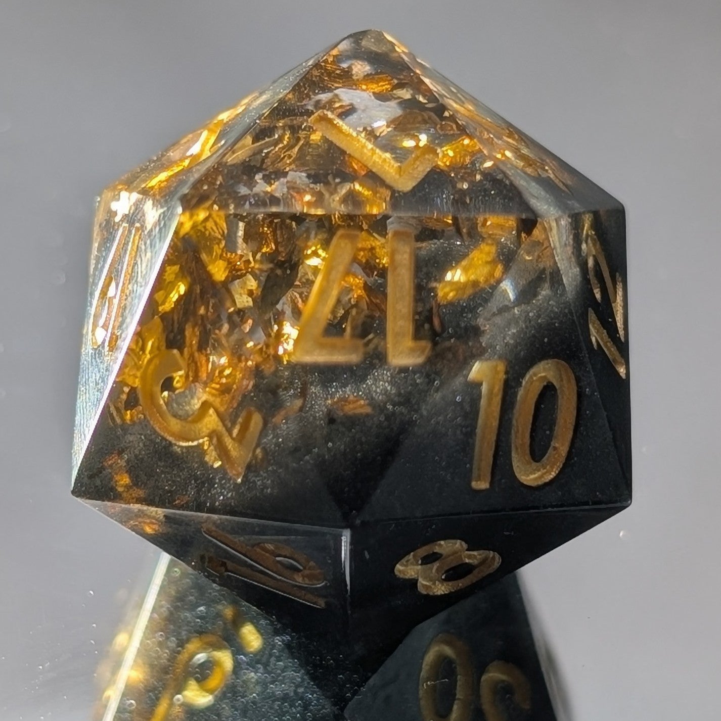 black and gold sharp edged d20 die on mirroed background showing a reflection on the bottom of the dice