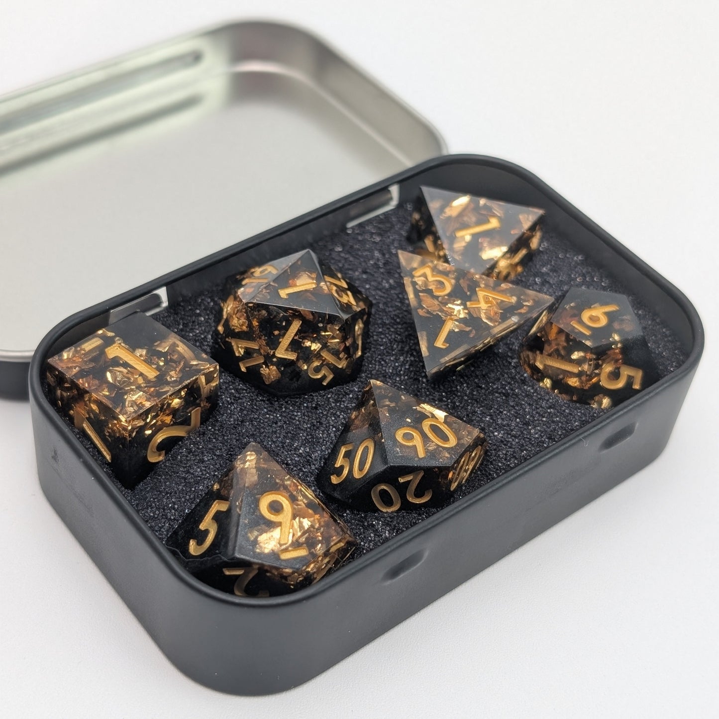 black and gold dice set with gold foil in metal dice tin on white background.