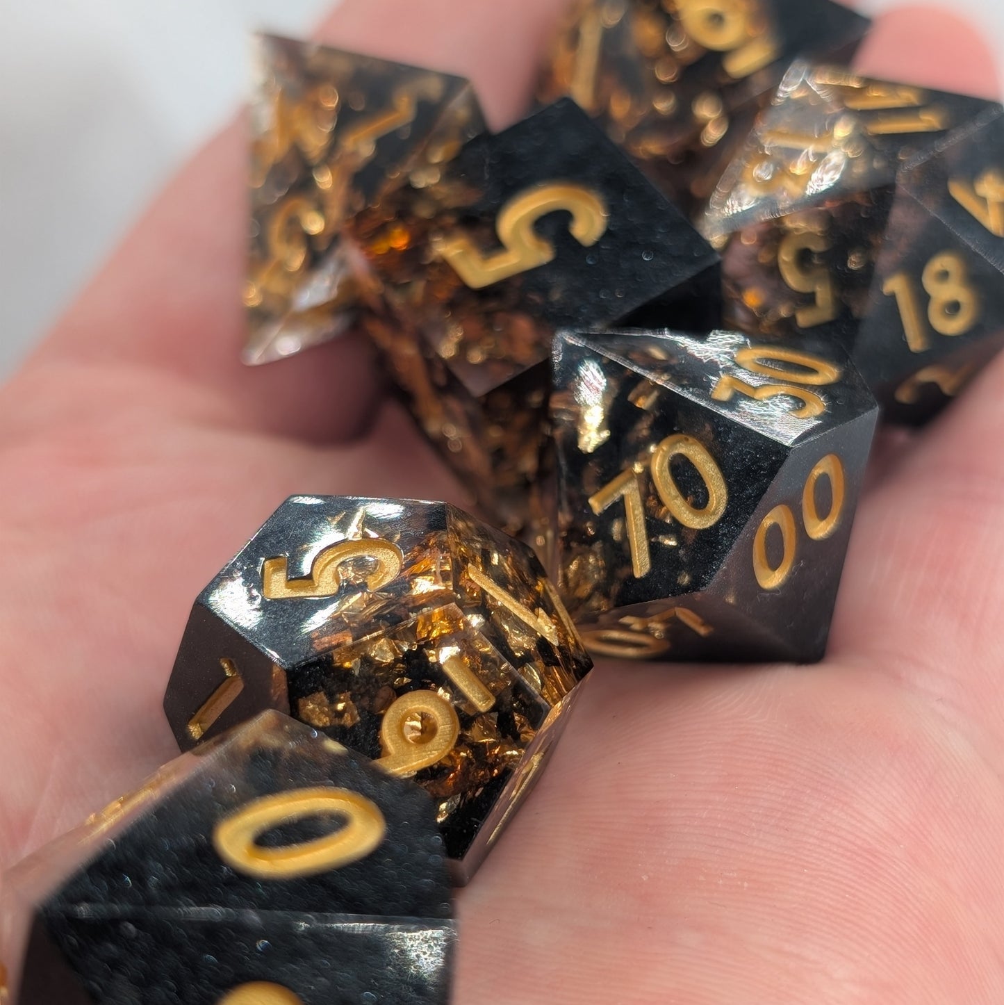black and gold numbered dnd dice set with gold ink numbers being held in hand with a close up shot in natural sun