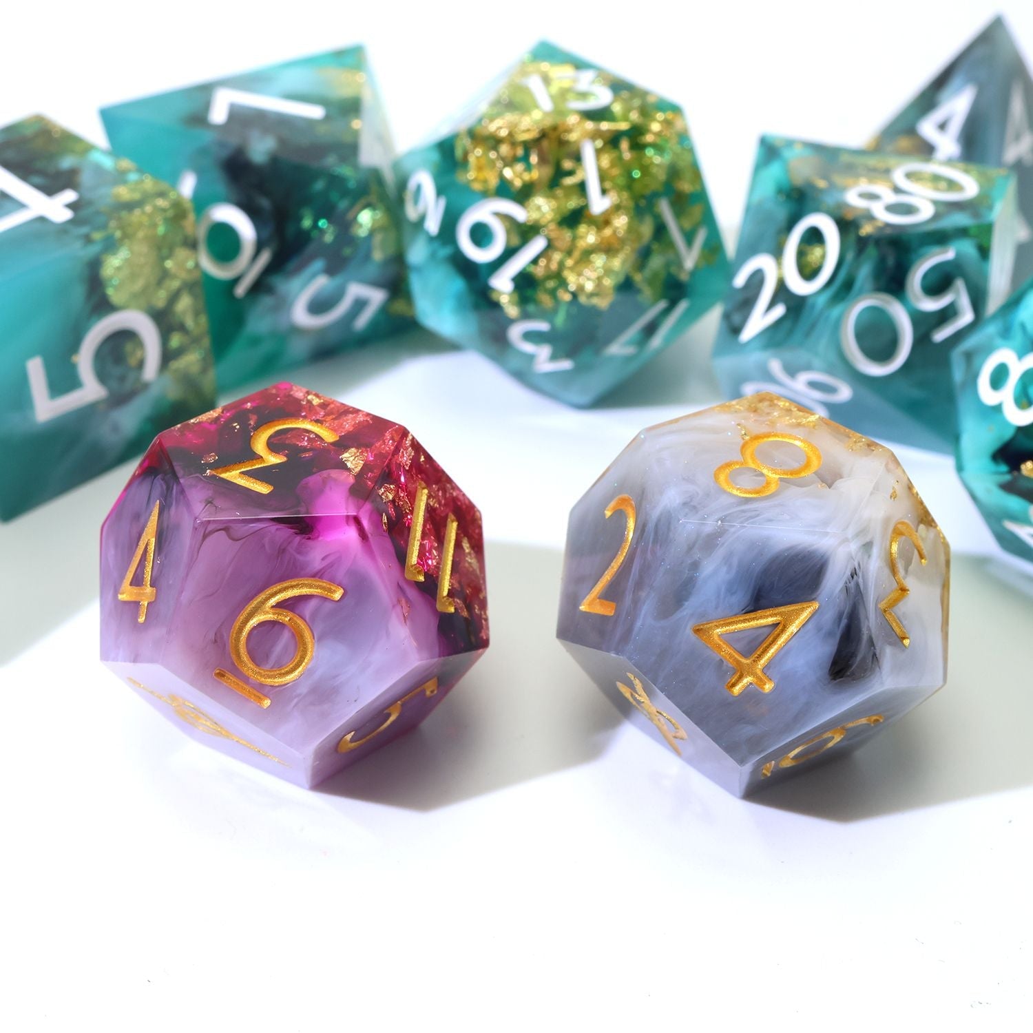 Daggerheart Dice Set on white background featuring a 7-Piece Green, black, with gold foil dice set and 2 duality dice in gold, white, pink and purple on a white background close up on the duality dice.