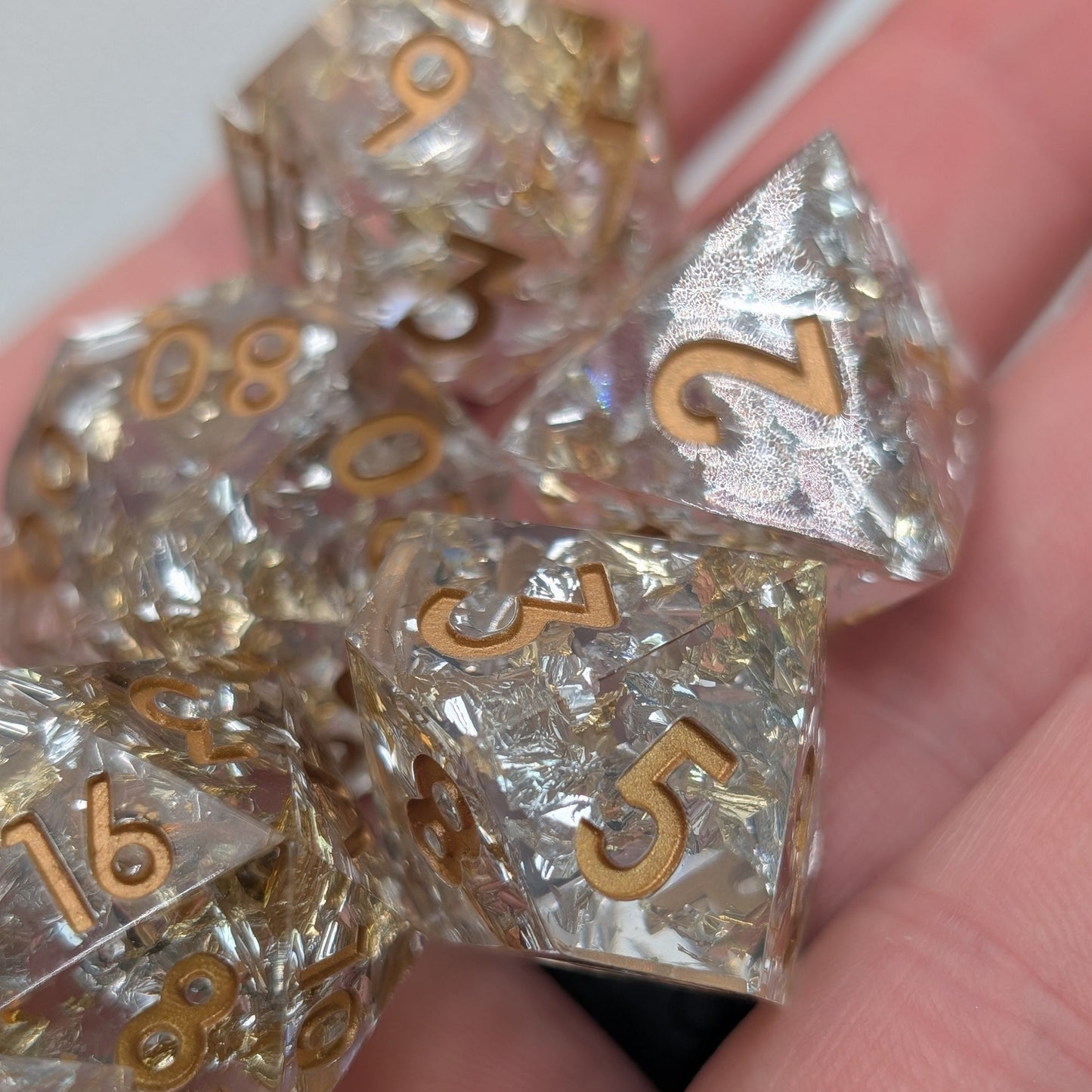 Close up of Emberlight Veil full 7-piece sharp-edge D&D dice set with gold and silver foil in hand