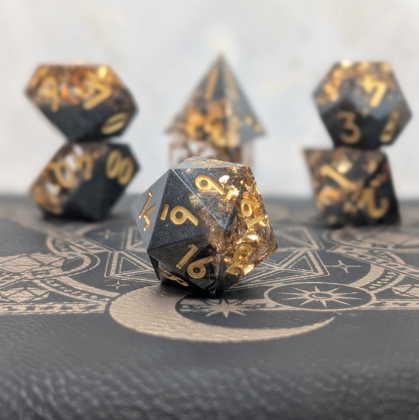 Obsidian Ember black and gold sharp edge resin dice set displayed on leather
