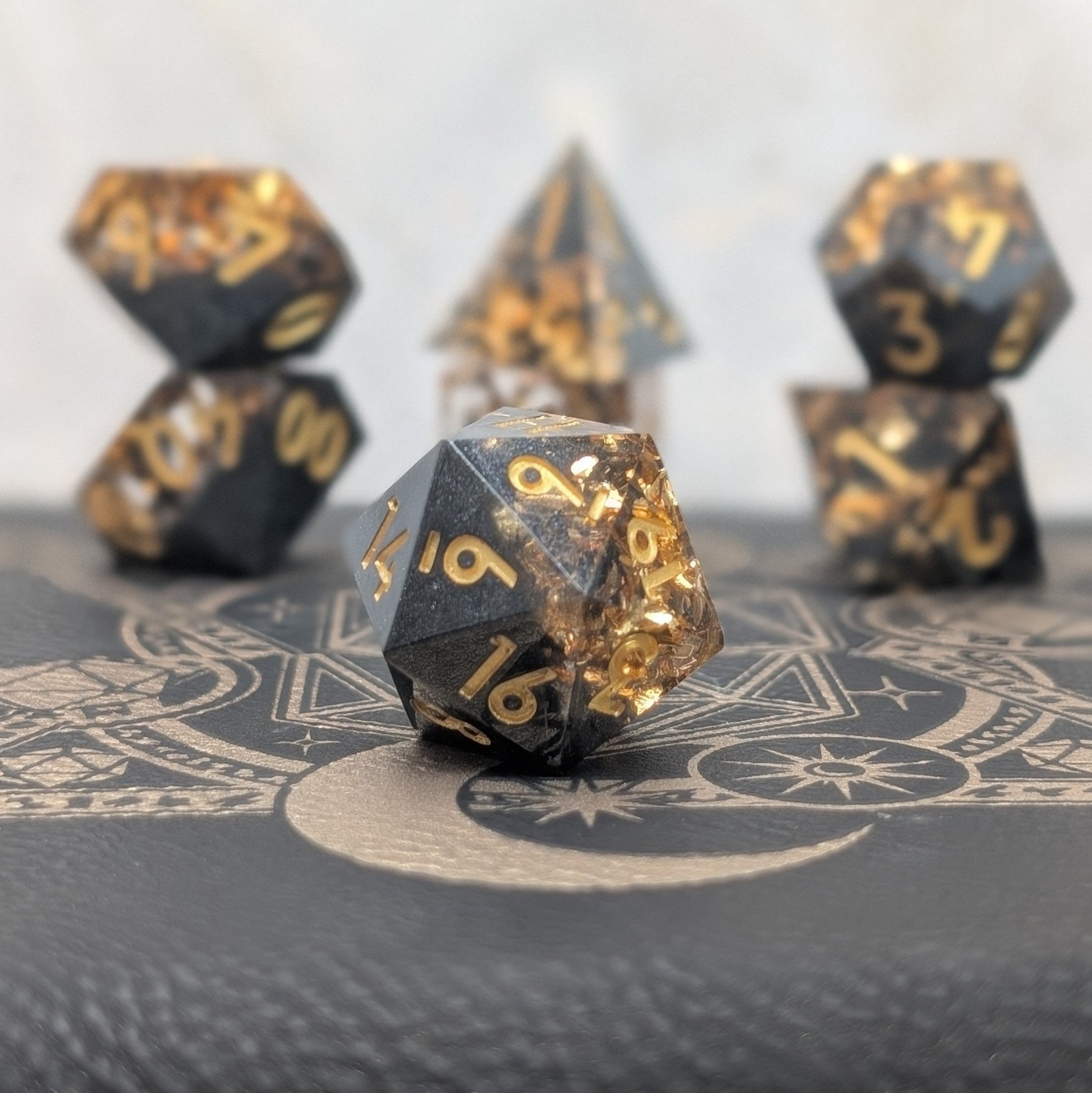 Obsidian Ember black and gold sharp edge resin dice set displayed on leather