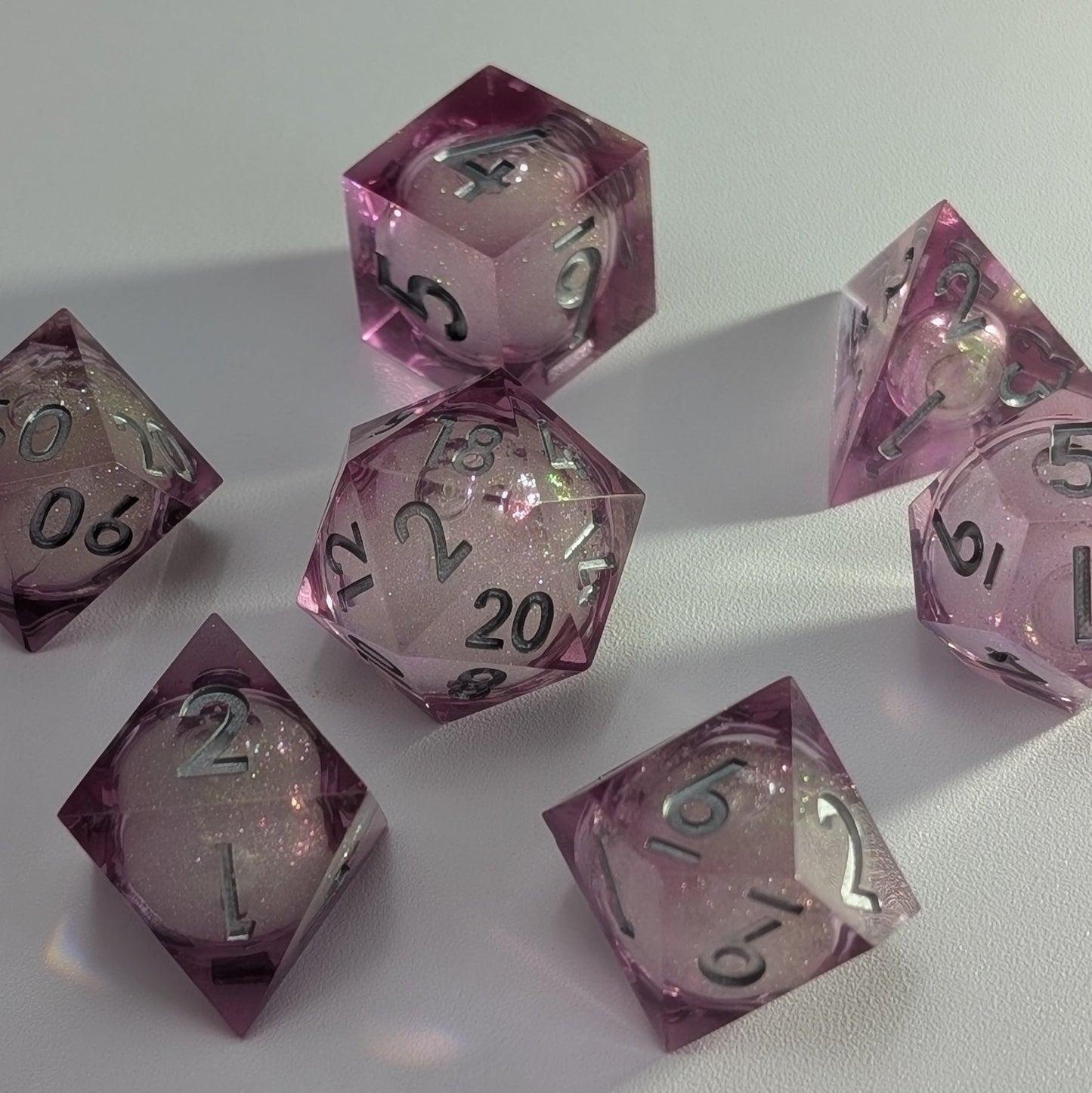 Sharp-edged pink DND dice set with a glittery liquid core and silver numbers, perfect for TTRPG sessions.