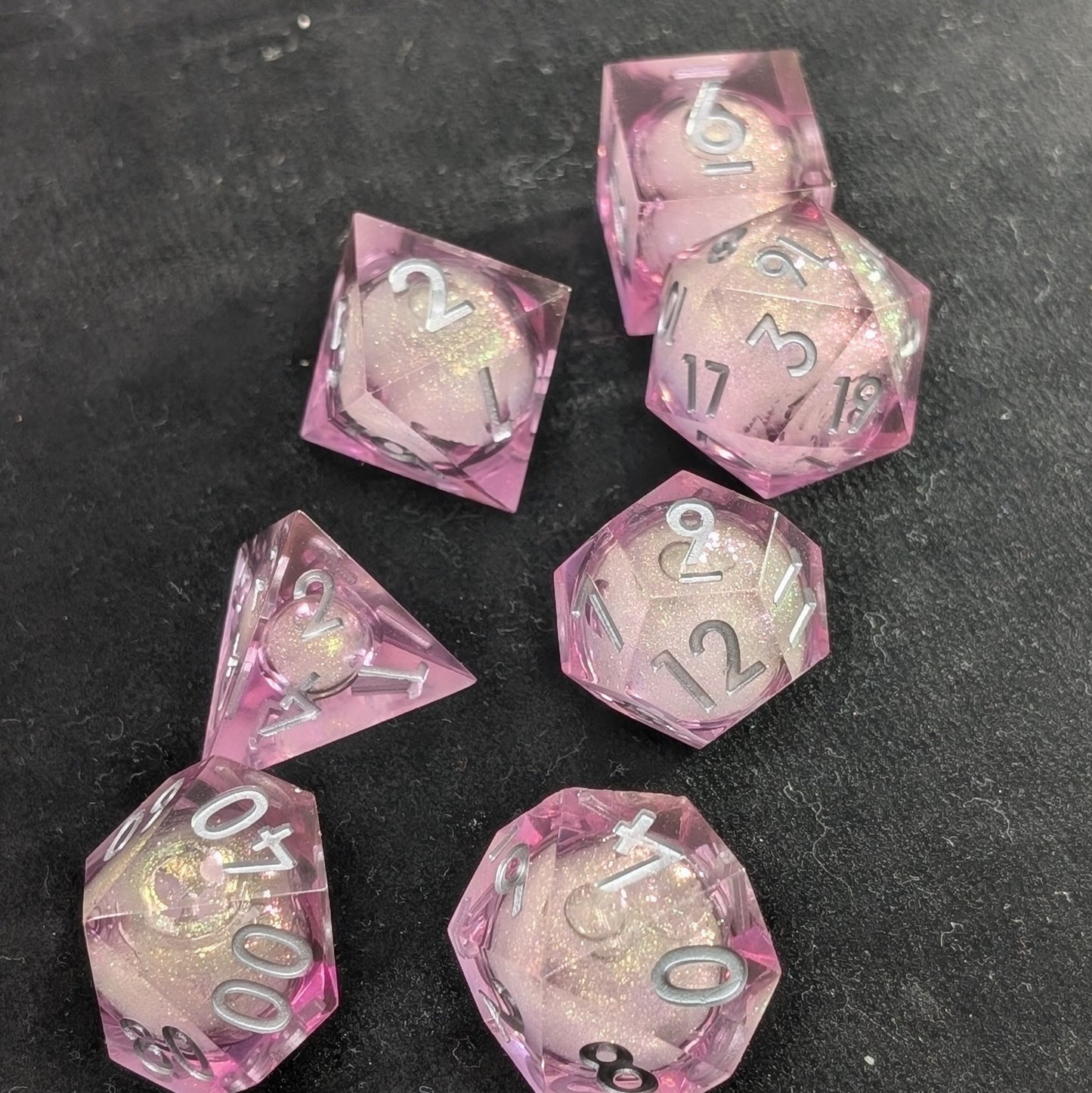 Handcrafted polyhedral dice set featuring translucent pink resin and a shimmering liquid center for roleplaying games on black background
