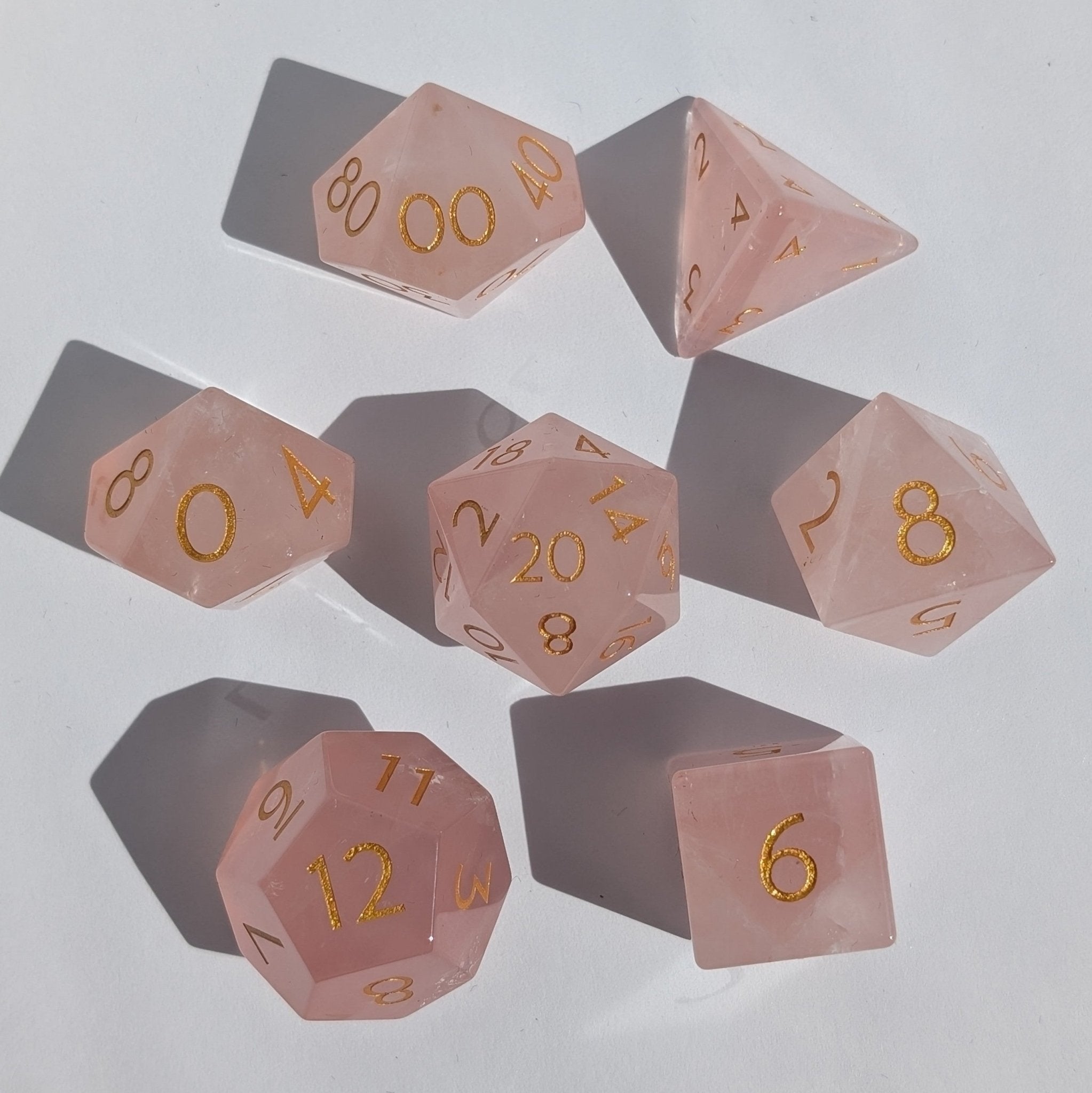 Set of pink polyhedral dice with gold numbers on a light gray background