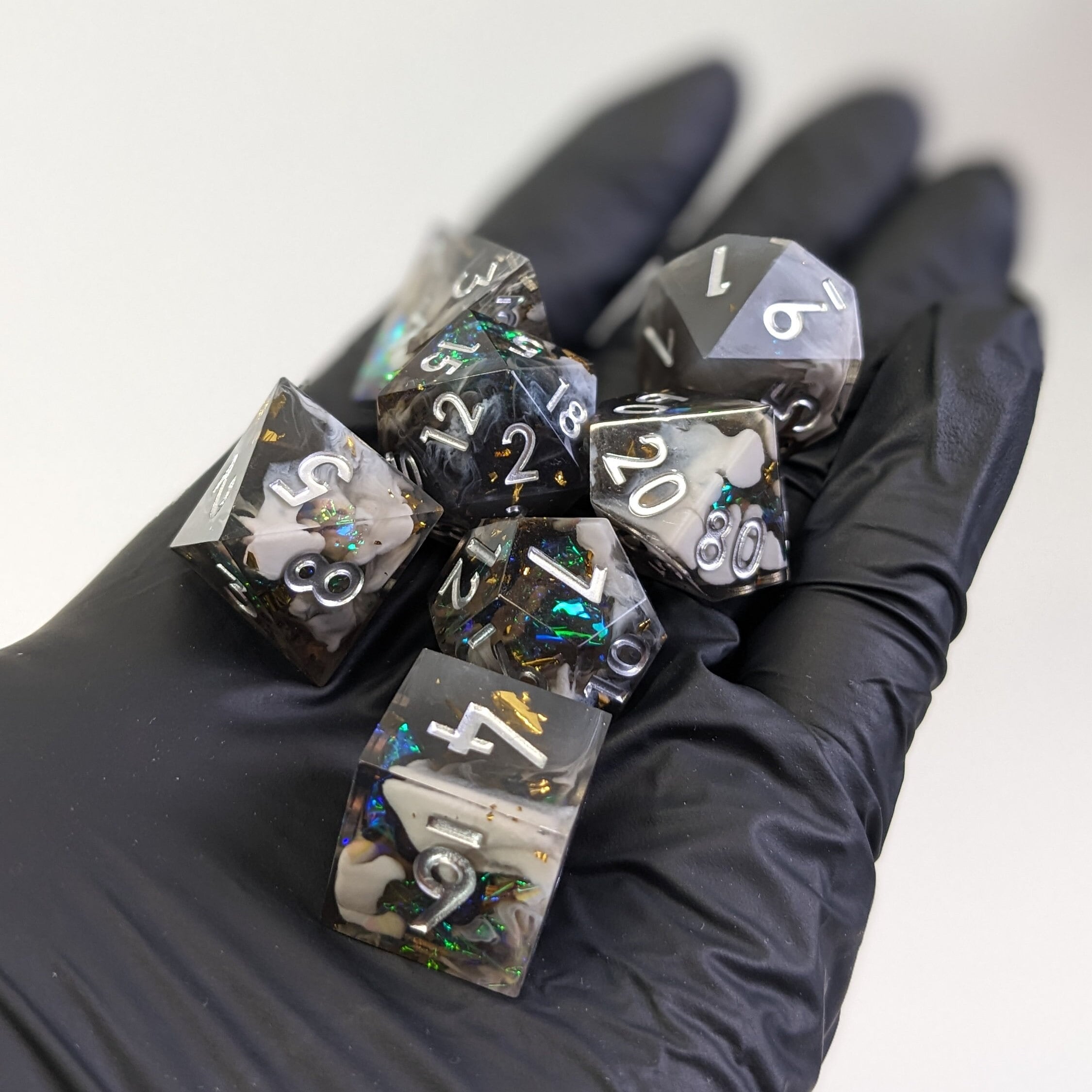 A set of multicolored, polyhedral dice held in a black glove, with intricate patterns and sharp edges visible.