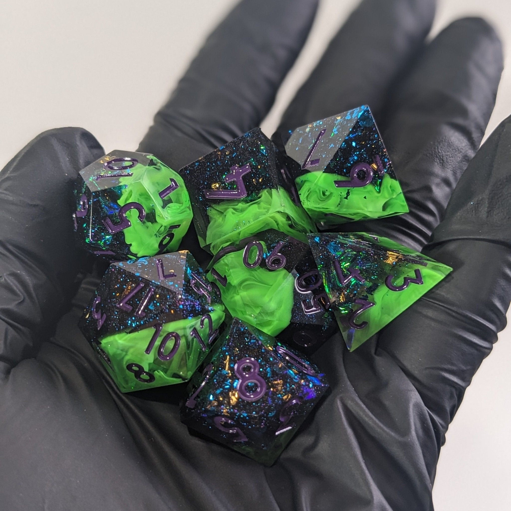 Green and black polyhedral dice set held in black gloves against a neutral background
