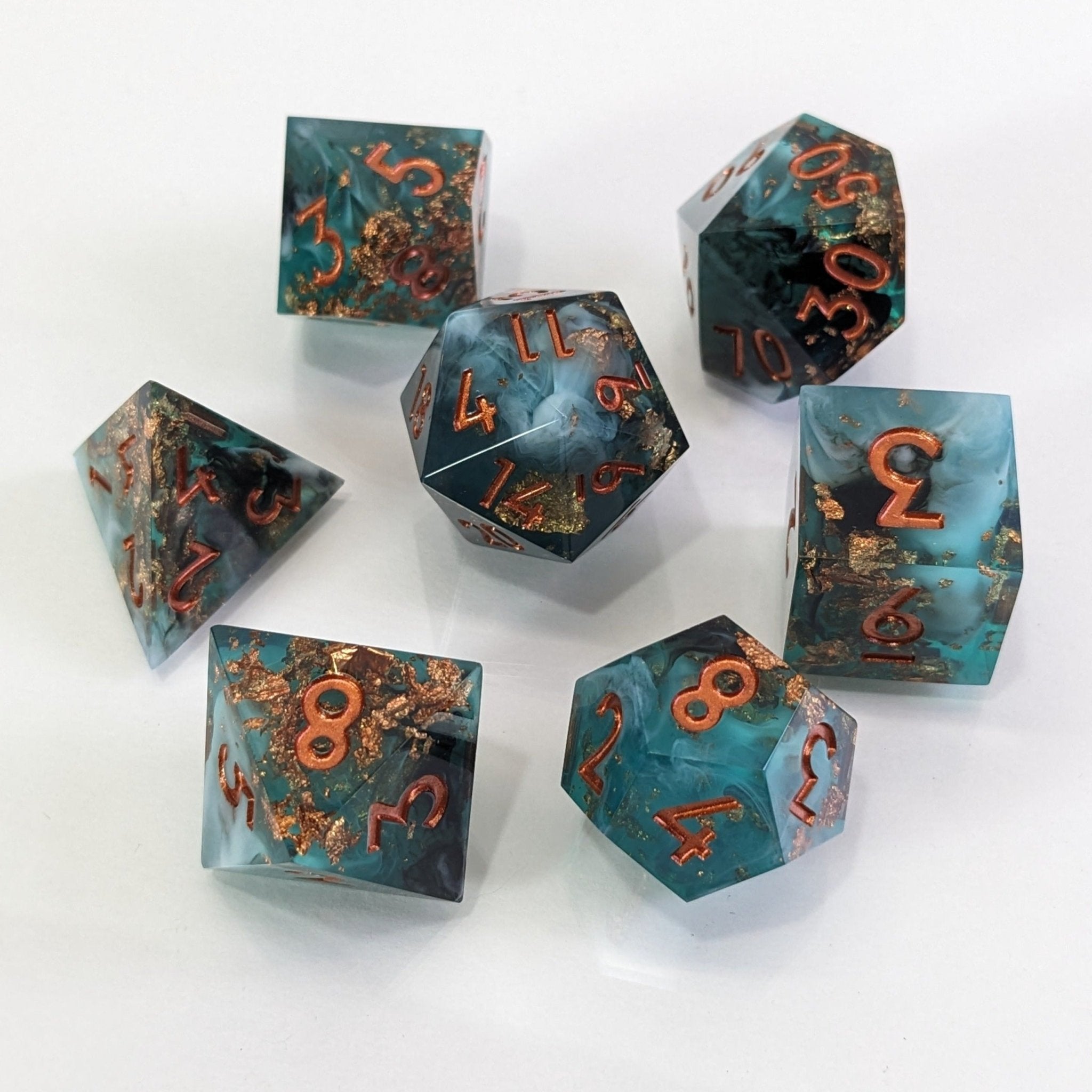 Aurora Azure Glintstone 7-Piece Polyhedral Dice Set. Sharp-Edged design featuring green, black, and white resin with copper leaf inclusions.