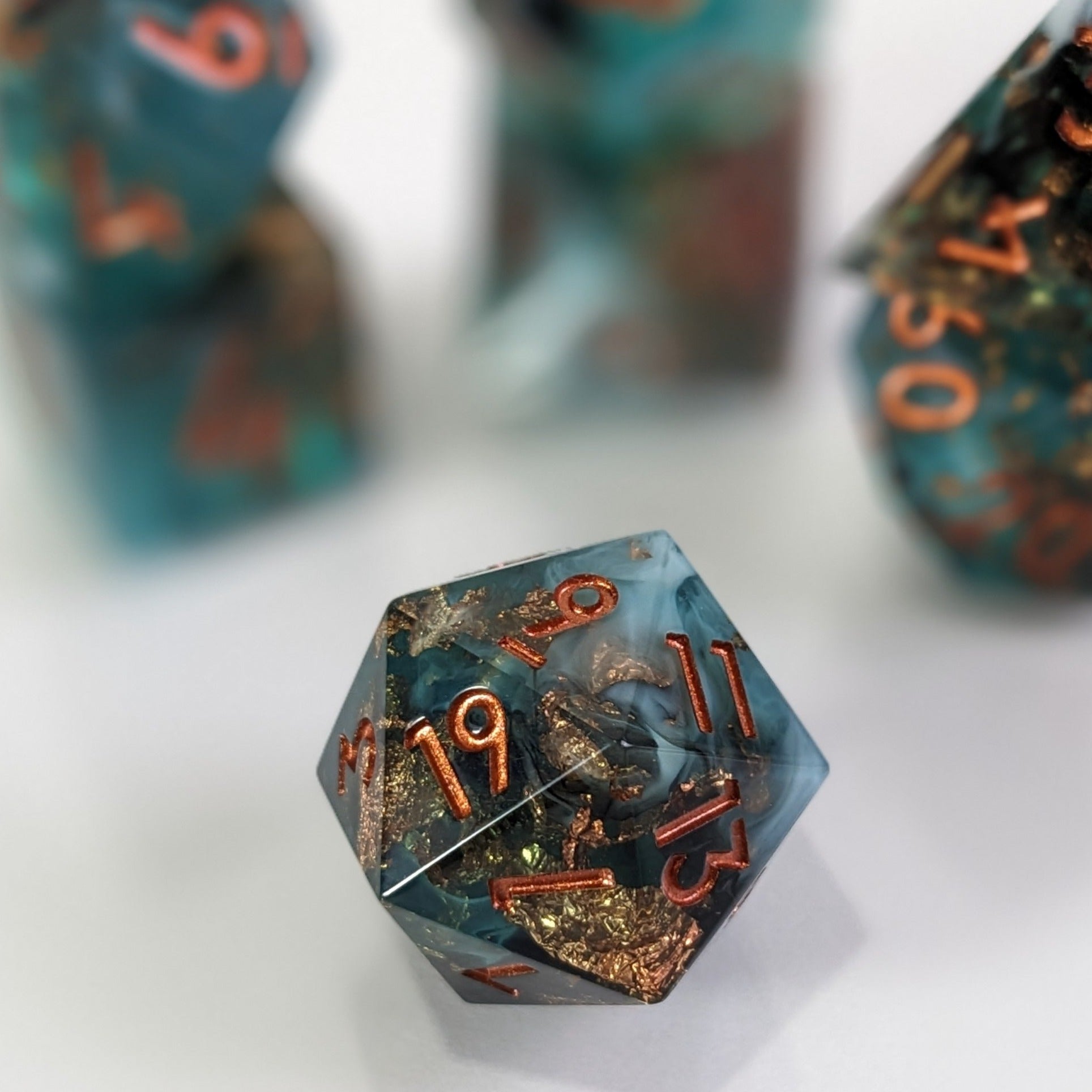 Green, Black, and White Sharp Edged Resin D20 with other dice out of focus in the back ground.