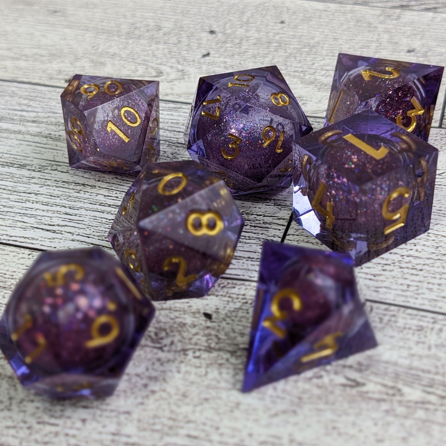 Purple liquid core dnd dice set with d4, d6, d8, d10, d%, d12, d20 adorned with gold numbers on rustic white wood backdrop.