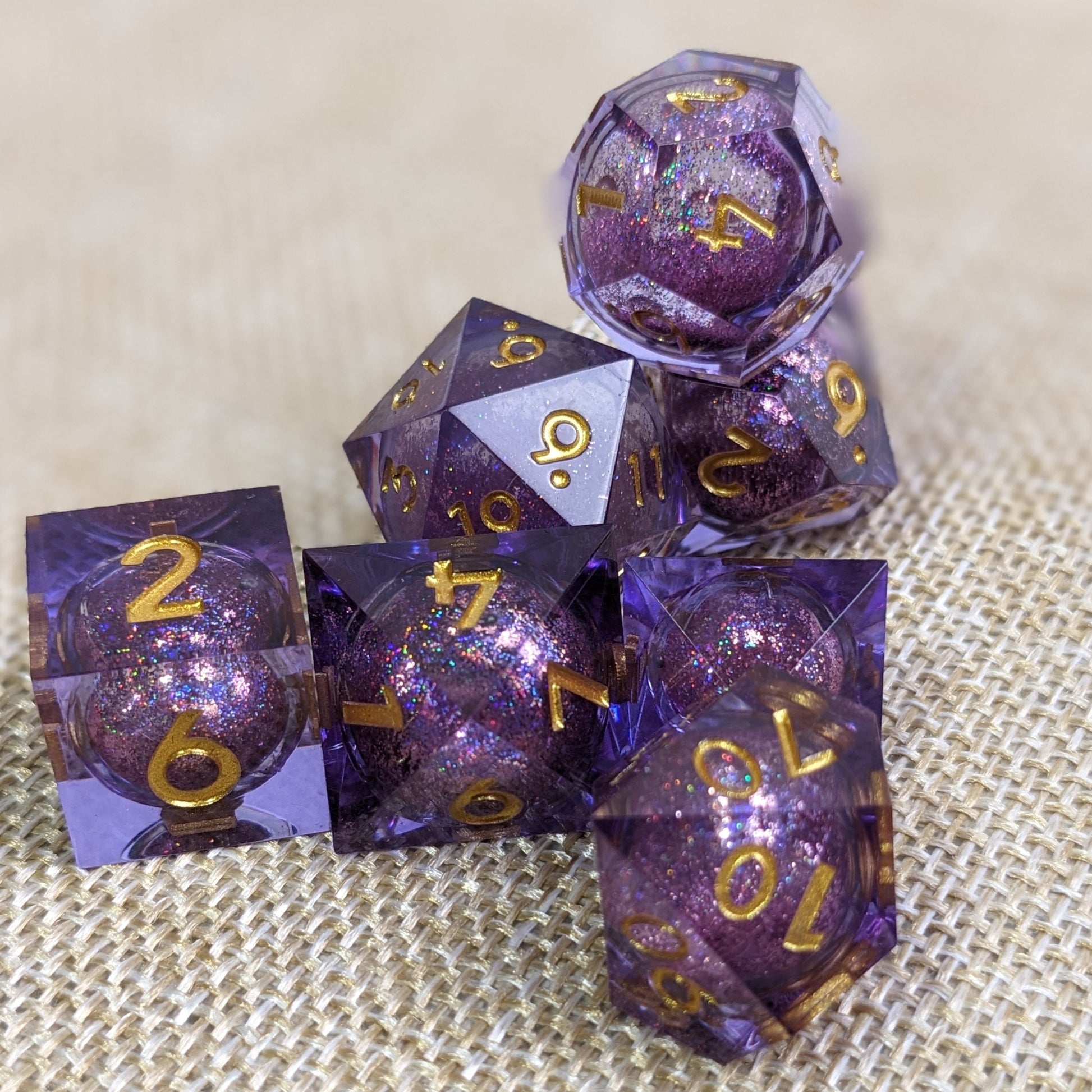 Full set of purple sharp edge resin dice with liquid cores stacked up on woven tan background 