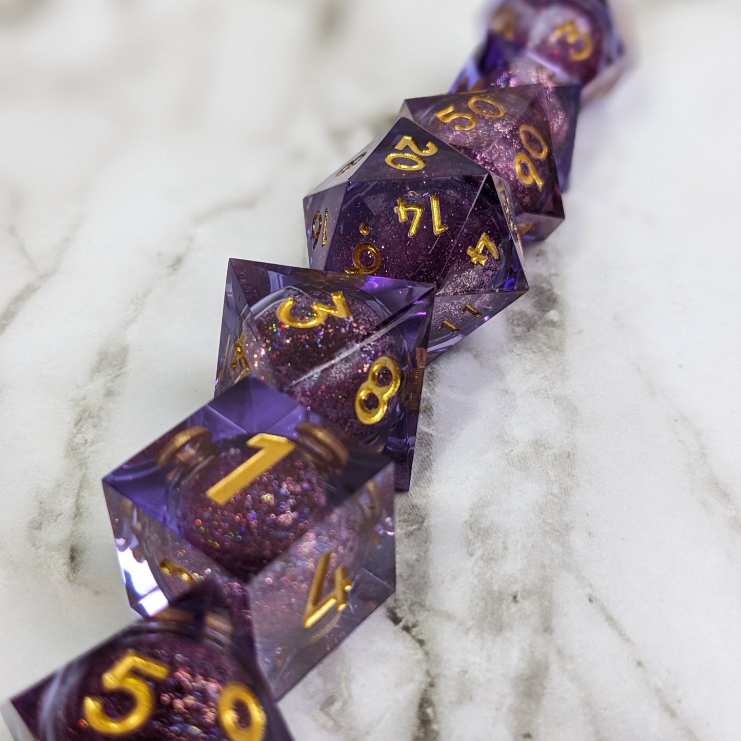 Gold numbered purple liquid core dice in a row on a marble backdrop