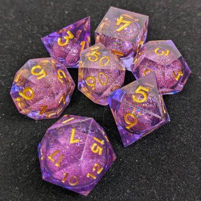 7 set of liquid core dice set made of purple resin, gold numbers and glitter core on black background 