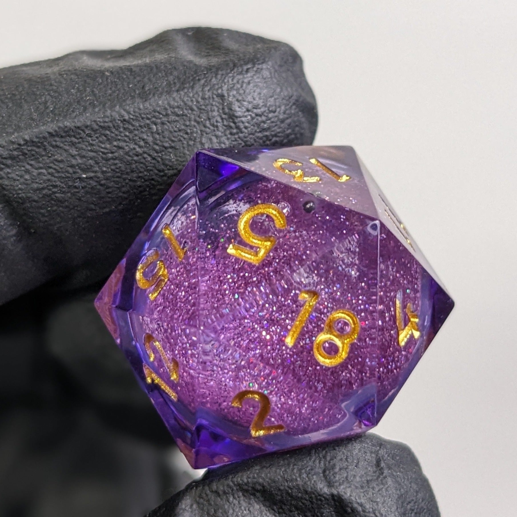 D20 Liquid Core Dice featuring purple resin and gold ink close up shot with black gloves