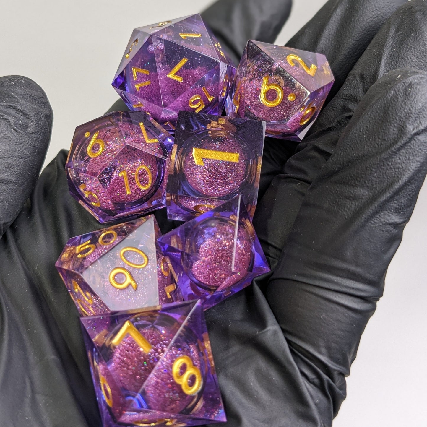 Full set of purple and gold liquid core dice being held in a hand with black gloves