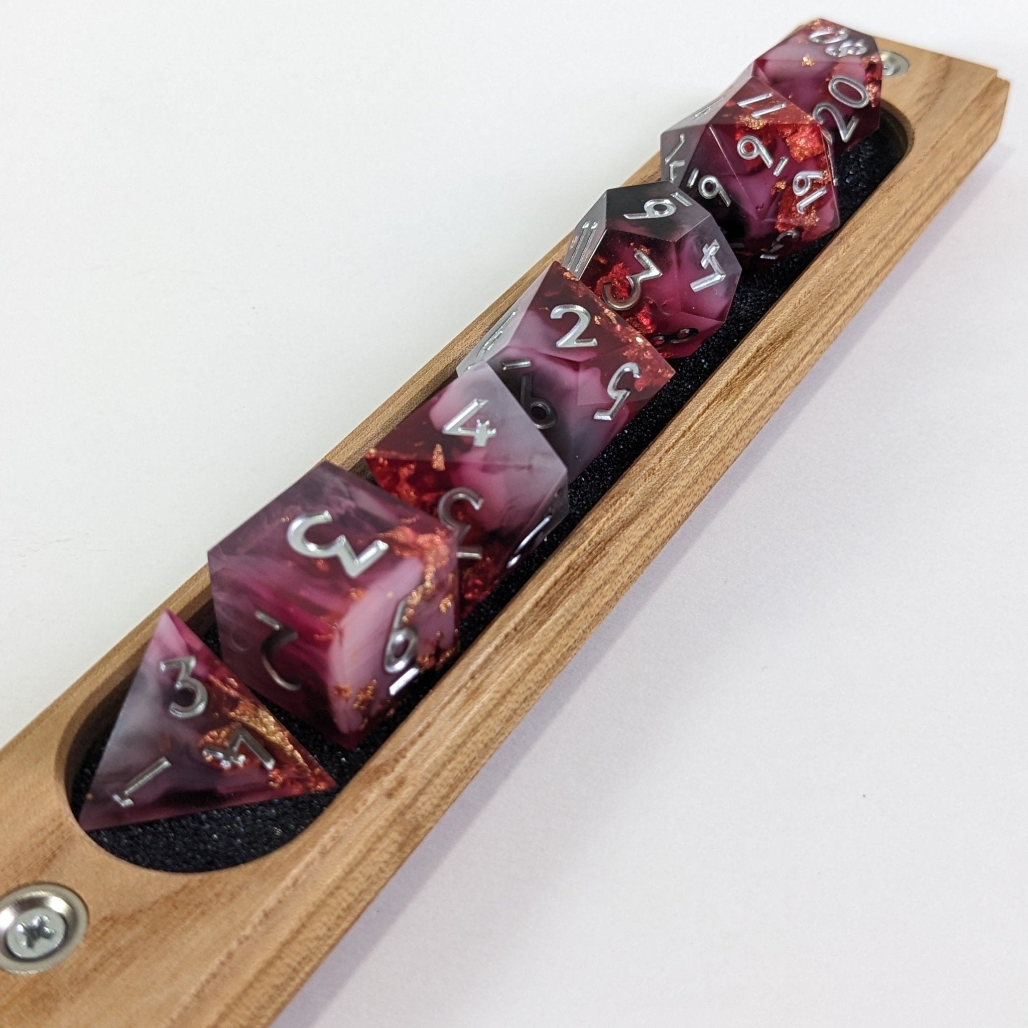 Set of purple polyhedral dice with numbers in a wooden holder on a white background