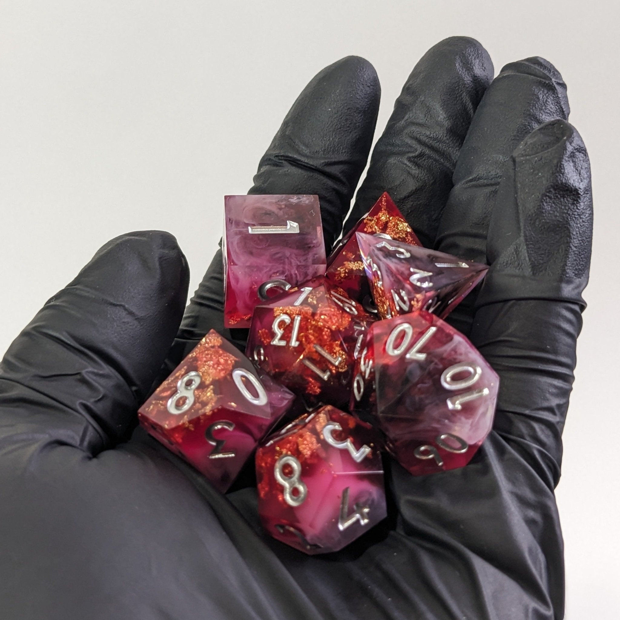 Black-gloved hands holding pink and red polyhedral dice against a white background