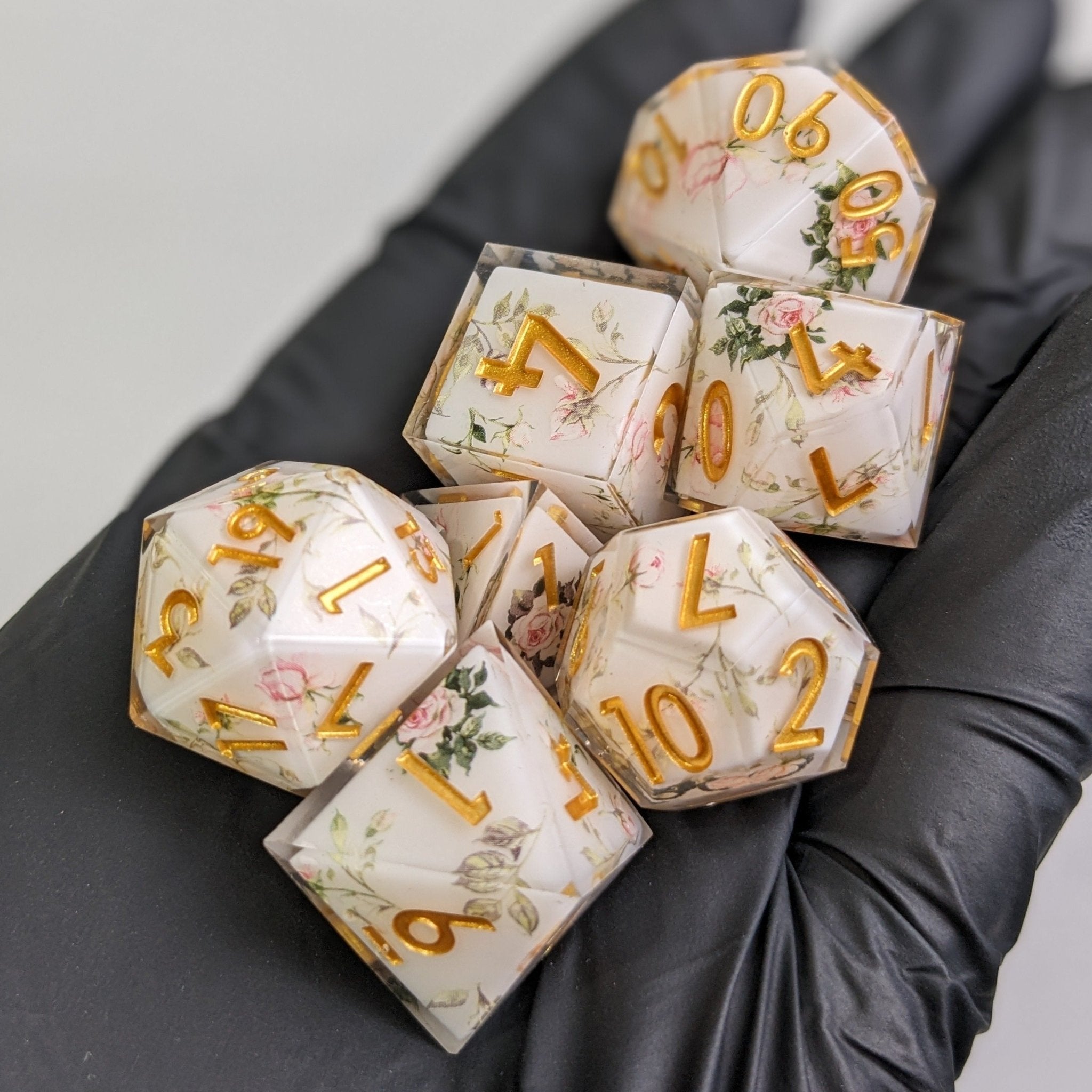 Set of decorative dice with floral patterns and gold numbers on a dark surface.