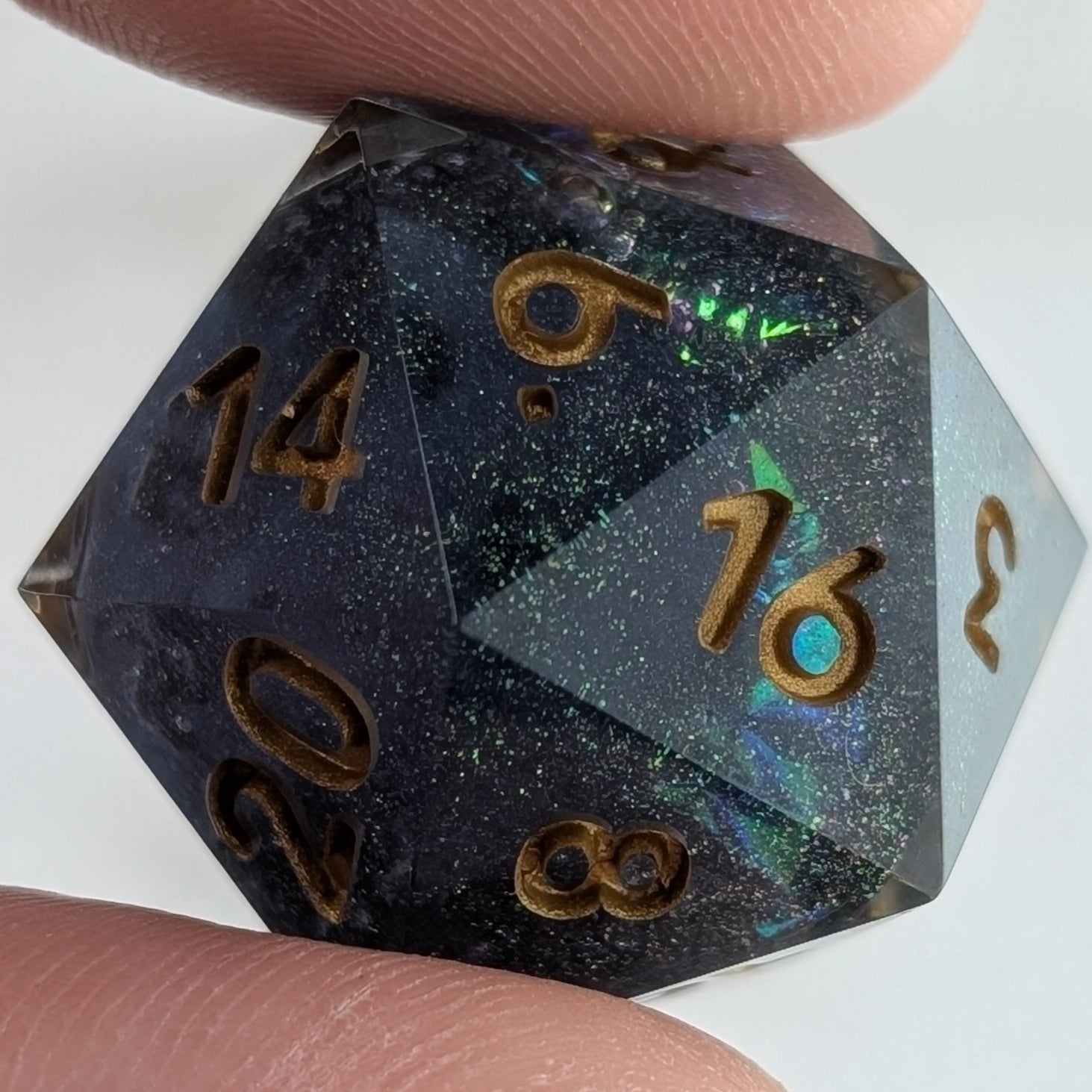 Black and Gold Sharp Edge D20 Dice being held between fingers on white background