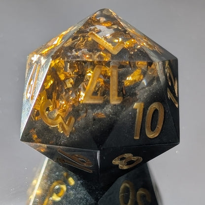 black and gold sharp edged d20 die on mirroed background showing a reflection on the bottom of the dice