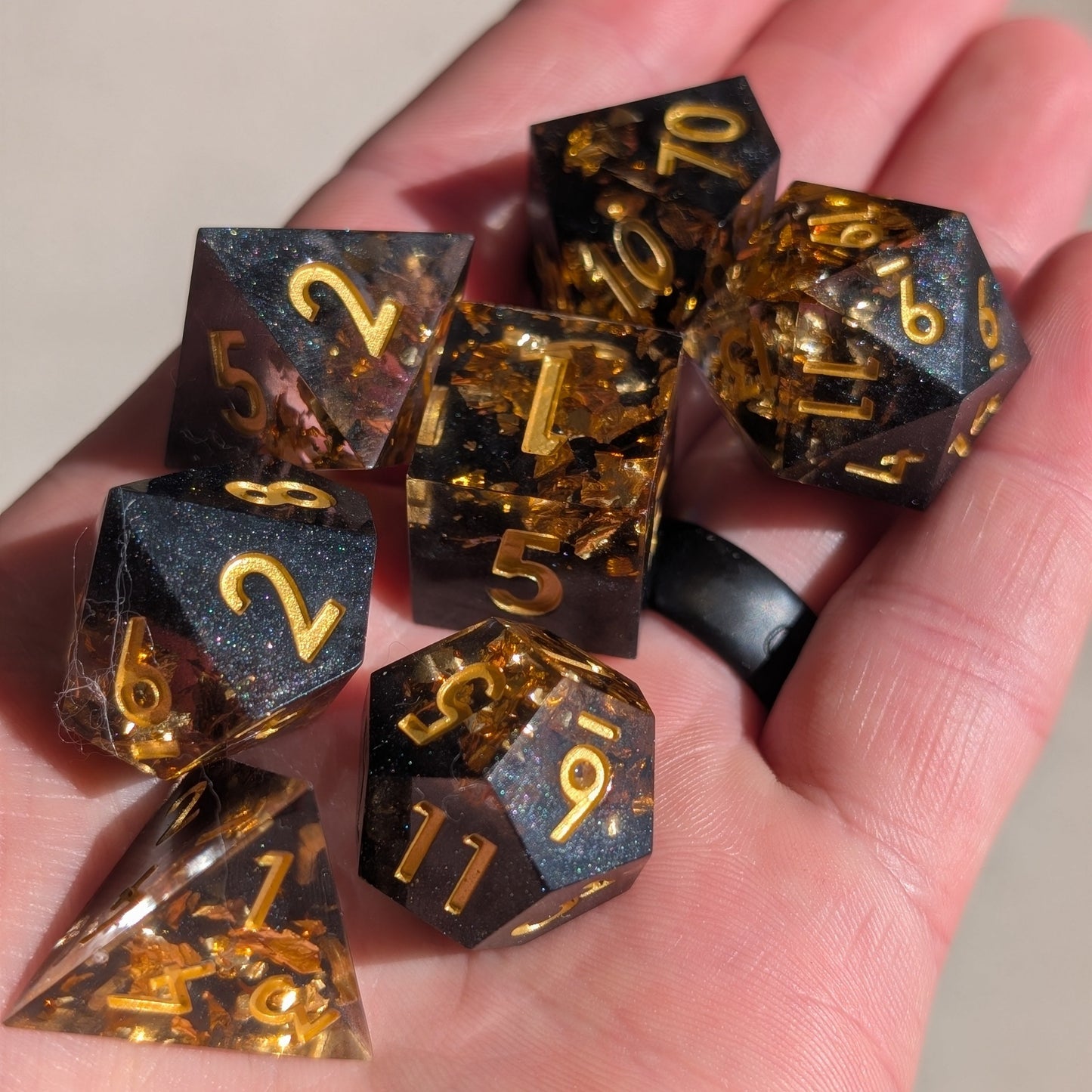 black and gold sharp edge dice set with gold numbers behind held in hand with natural sun light.