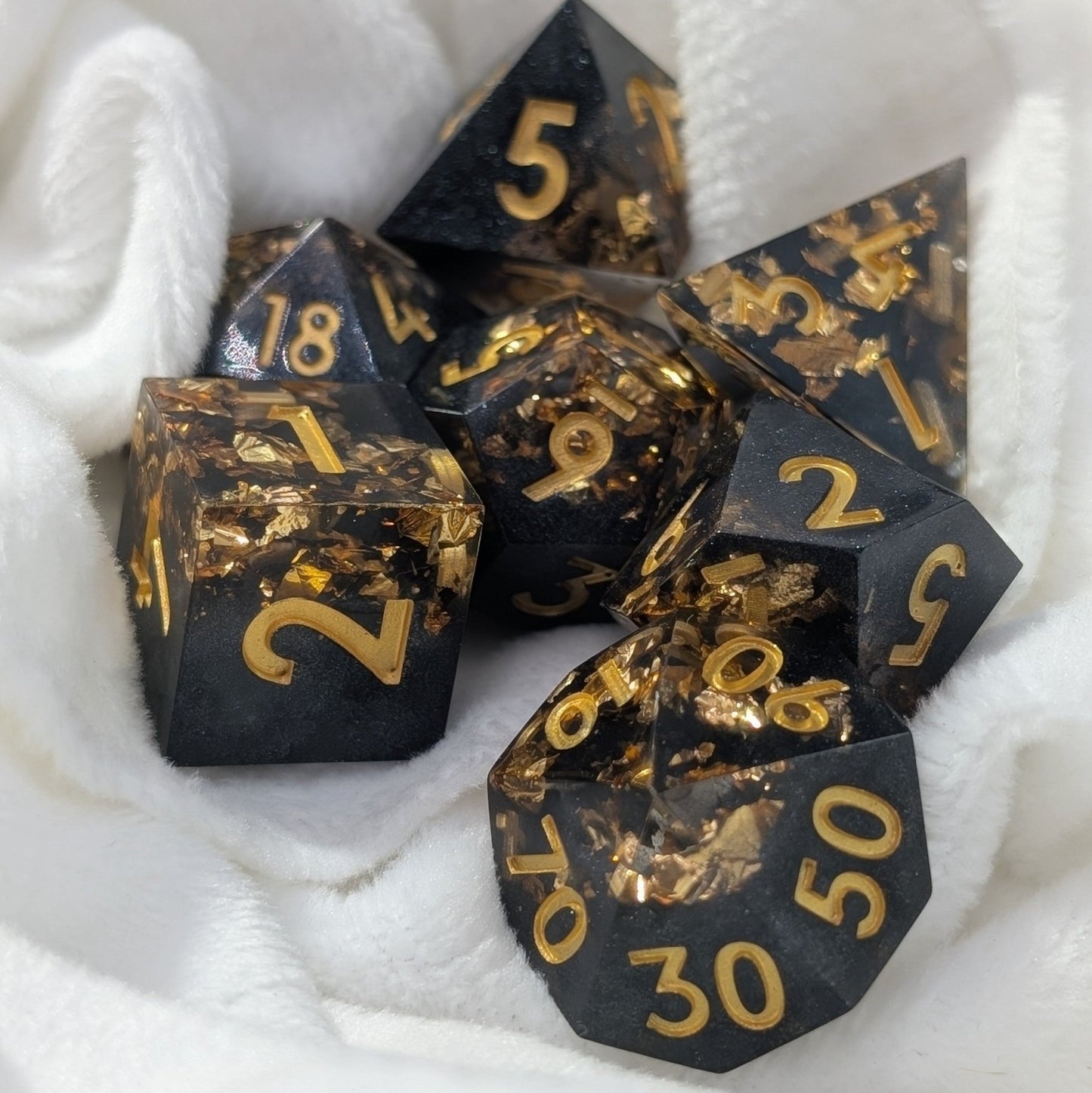 black and gold sharp edged polyhedral dice set used in dungeons & dragons and other ttrpg games on a white cloth background
