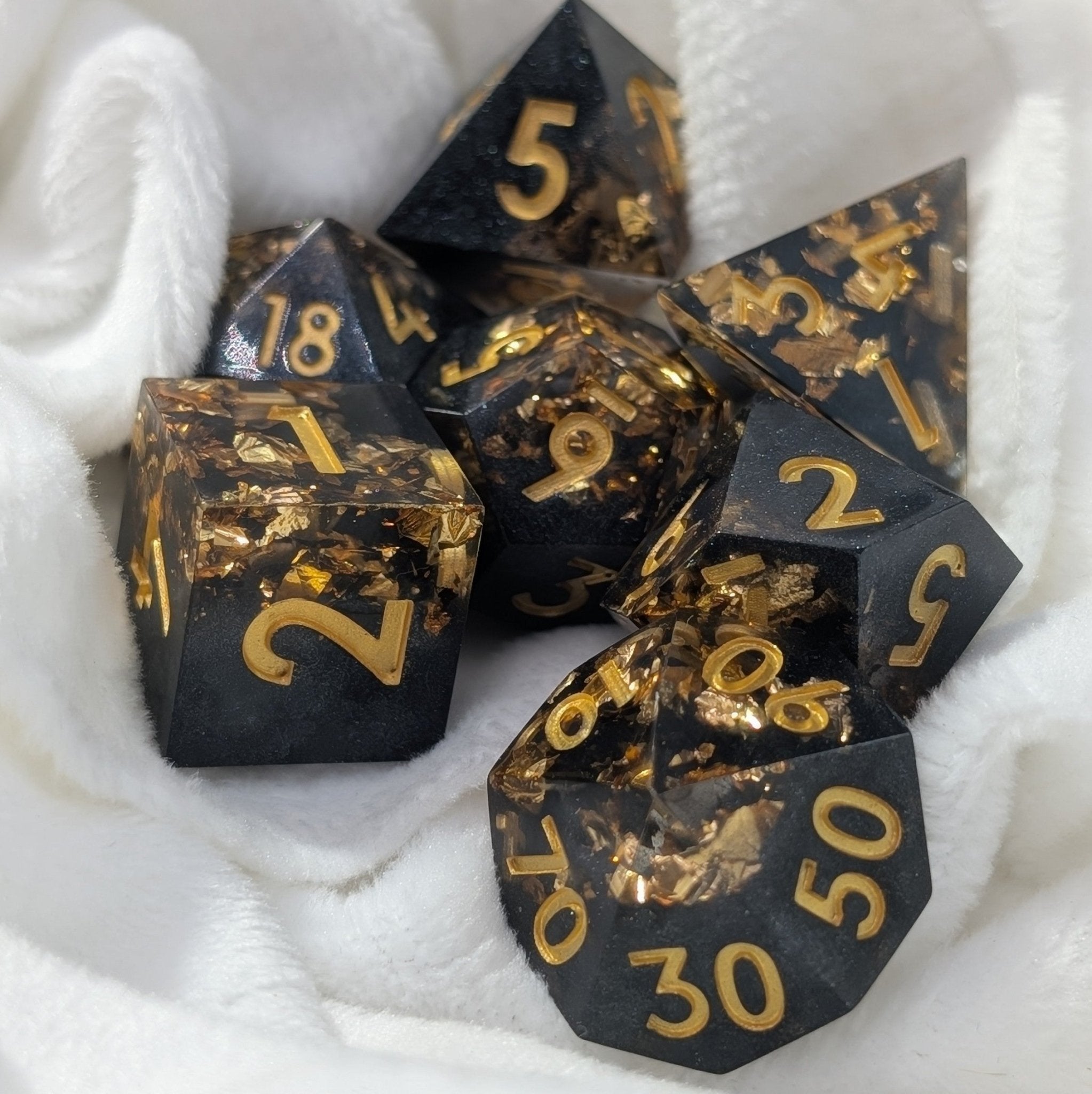 black and gold sharp edged polyhedral dice set used in dungeons & dragons and other ttrpg games on a white cloth background