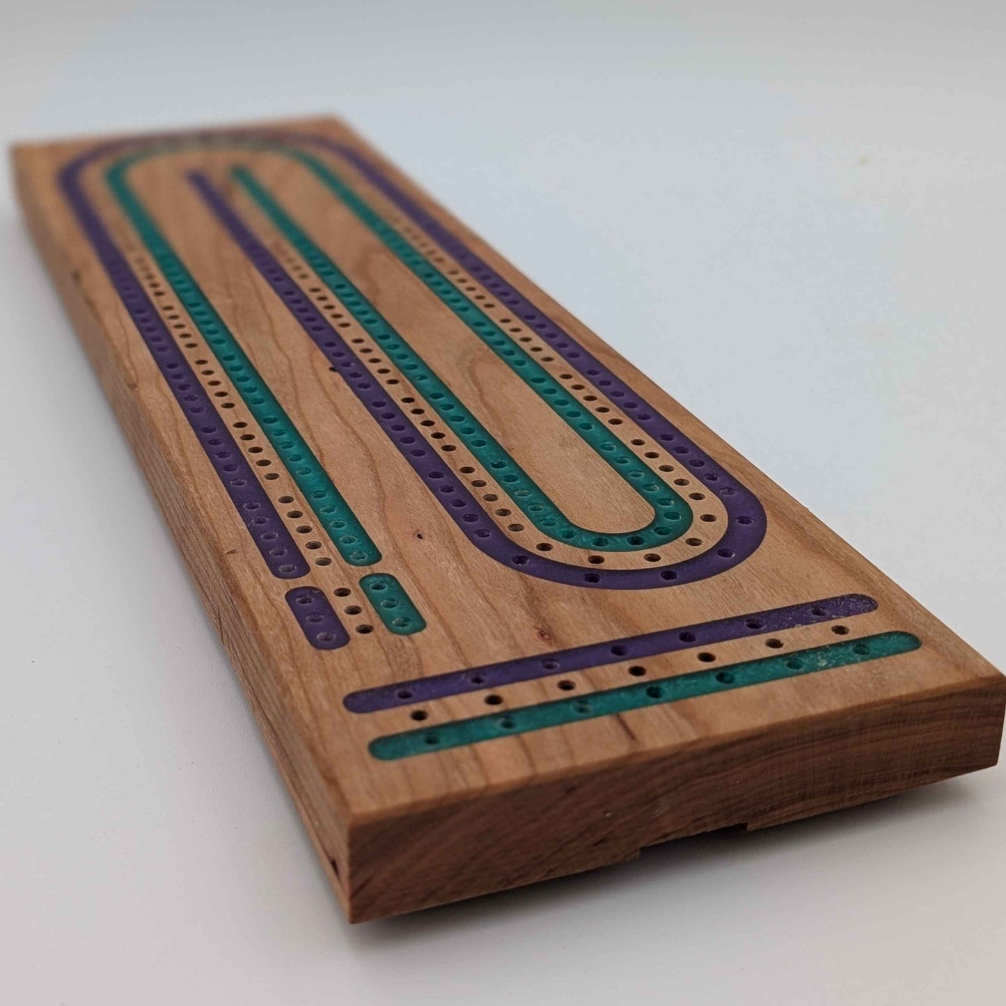 Handcrafted Cribbage board made of cherry wood featuring a 3 track resin inlay of purple and green tracks on white background