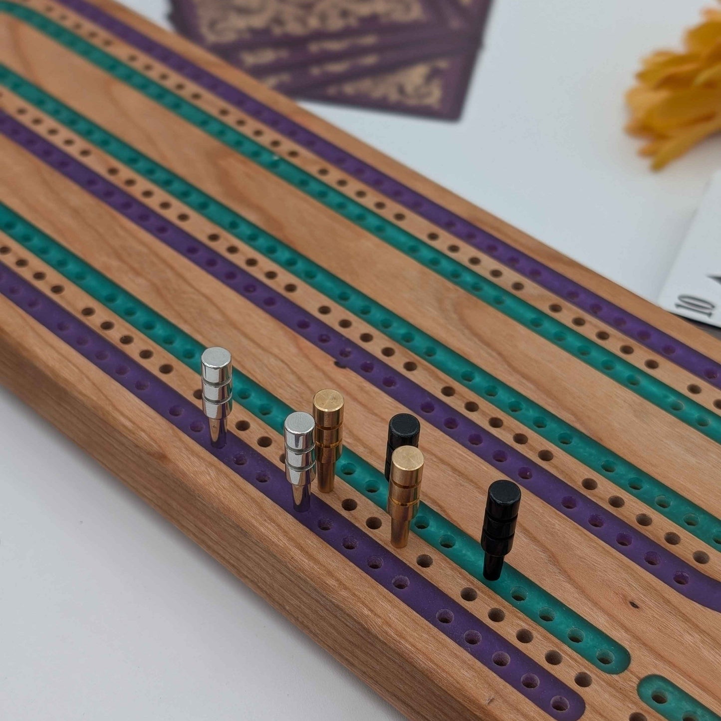 Handcrafted Cribbage board made of cherry wood featuring a 3 track resin inlay of purple and green tracks shot from side of board