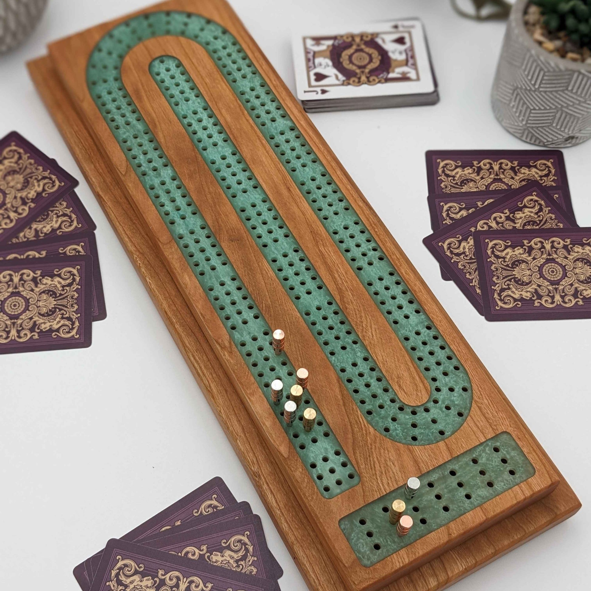 cherry wood cribbage board with emerald resin inlay with pegs and cards on white background