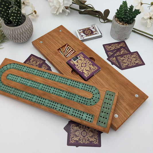 handmade cribbage board with card storage and peg storage made of cherry wood with emerald resin inlay showing off the magentic enclosure with top and bottom of cribbage board split.