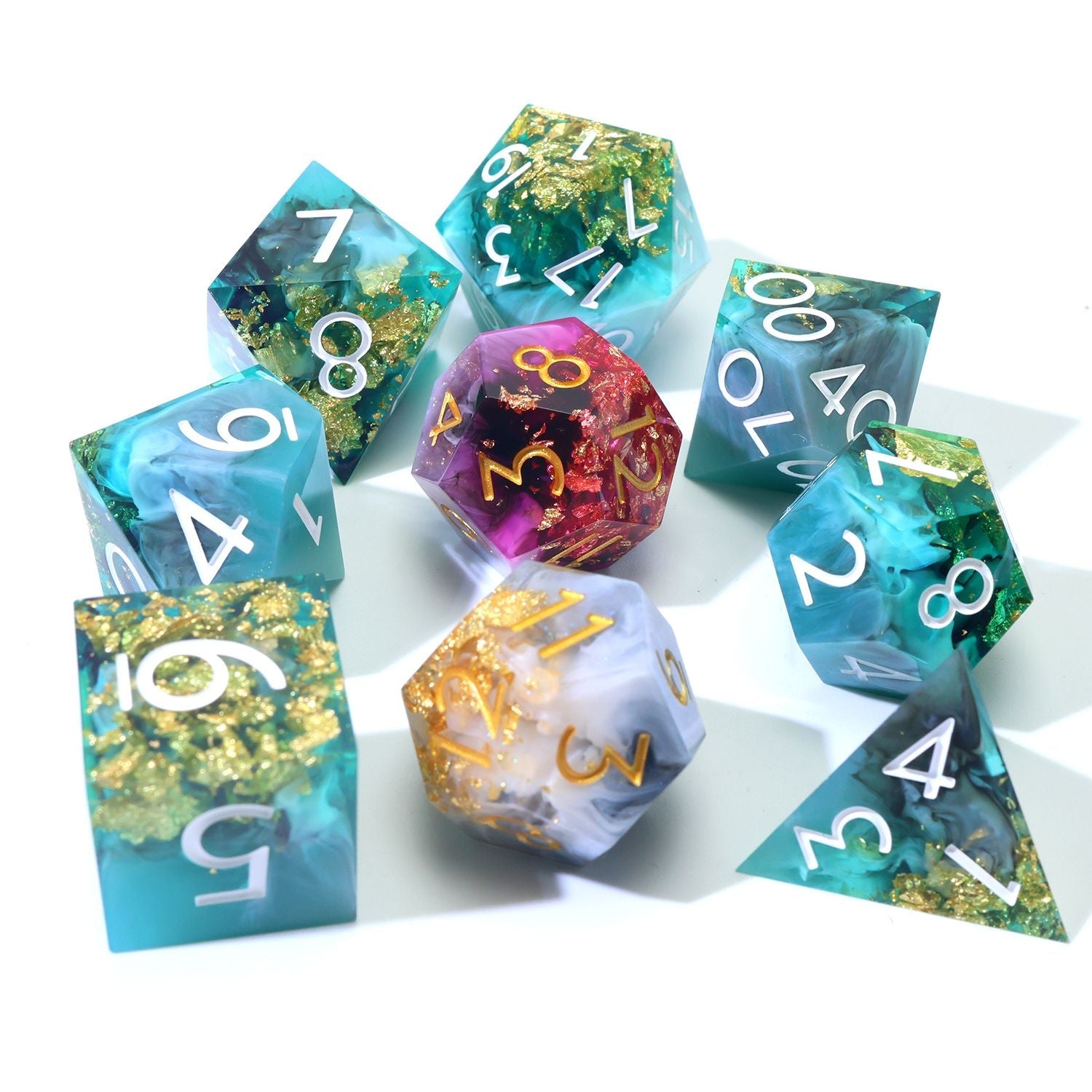 Daggerheart Dice Set on white background featuring a 7-Piece Green, black, with gold foil dice set and 2 duality dice in gold, white, pink and purple on a white background clustered with duality dice in the center.