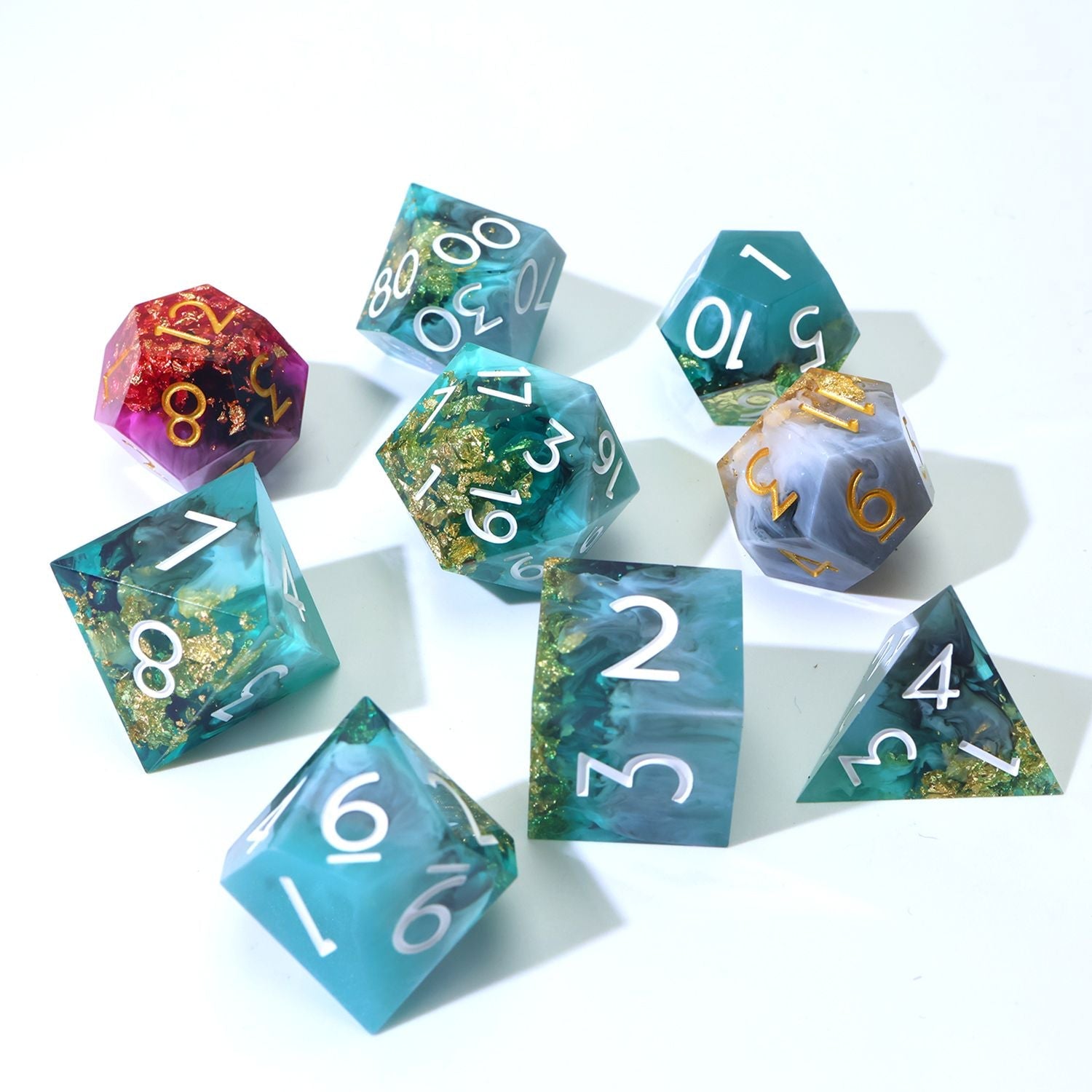 Daggerheart Dice Set on white background featuring a 7-Piece Green, black, with gold foil dice set and 2 duality dice in gold, white, pink and purple on a white background spread out.