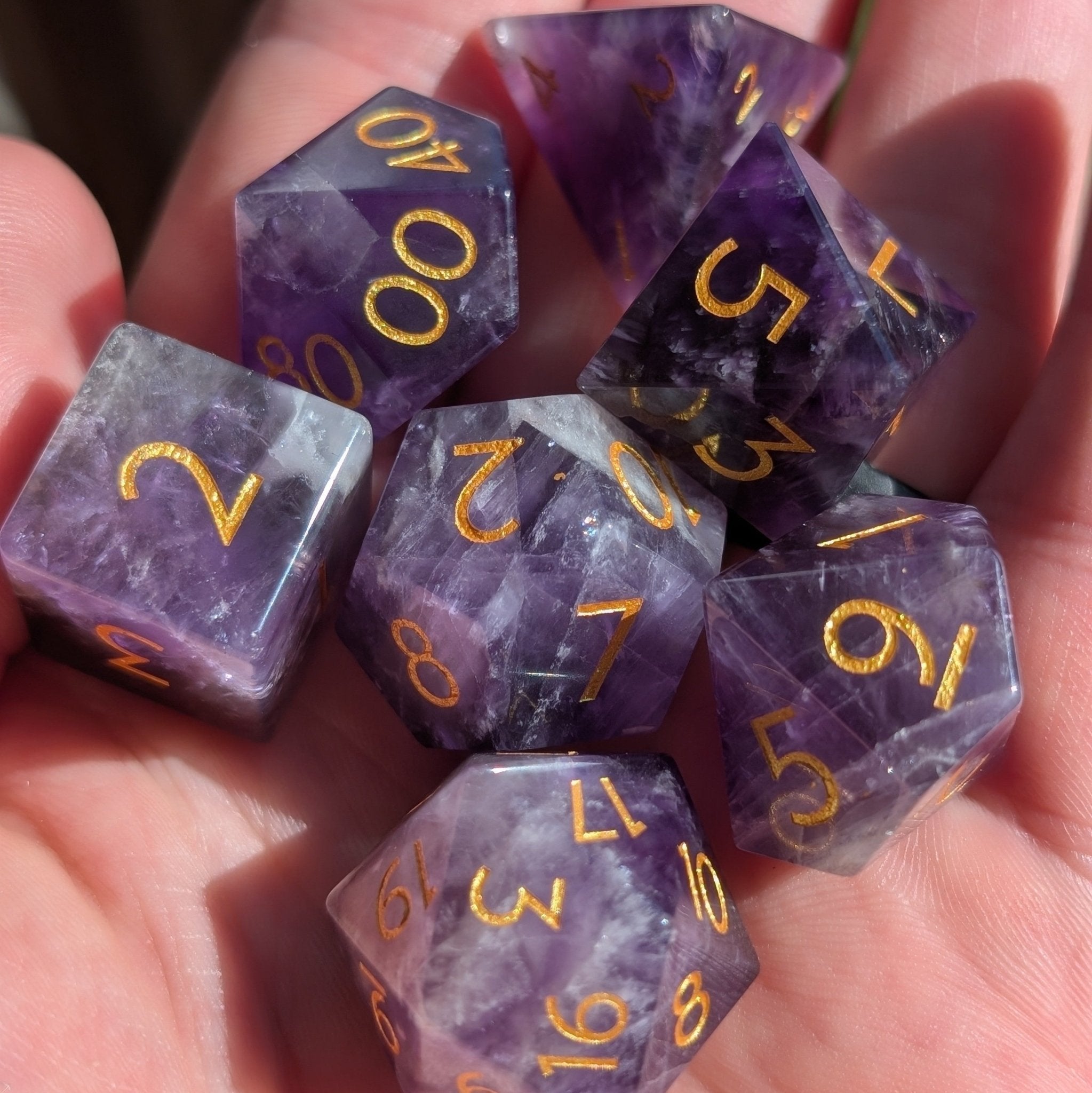Close-up of a hand holding Ebonwood's genuine Amethyst D&D dice set, showcasing the luxurious feel, deep violet hues, and minimalist gold-inked numbers of the natural gemstone.