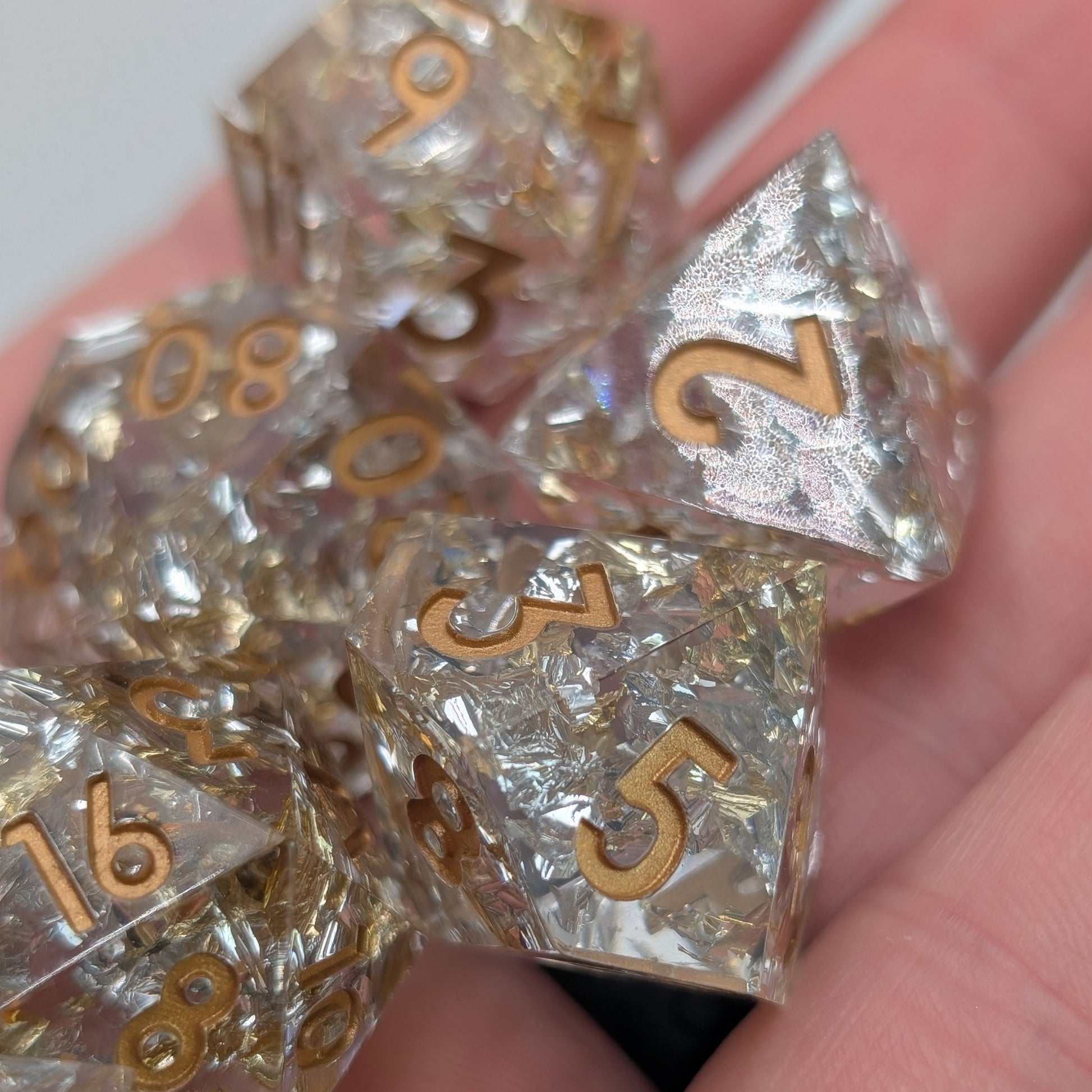Close up of Emberlight Veil full 7-piece sharp-edge D&D dice set with gold and silver foil in hand