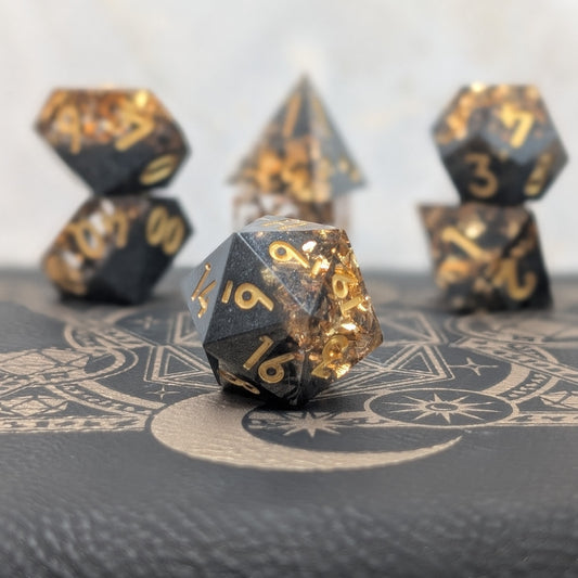 Obsidian Ember black and gold sharp edge resin dice set displayed on leather