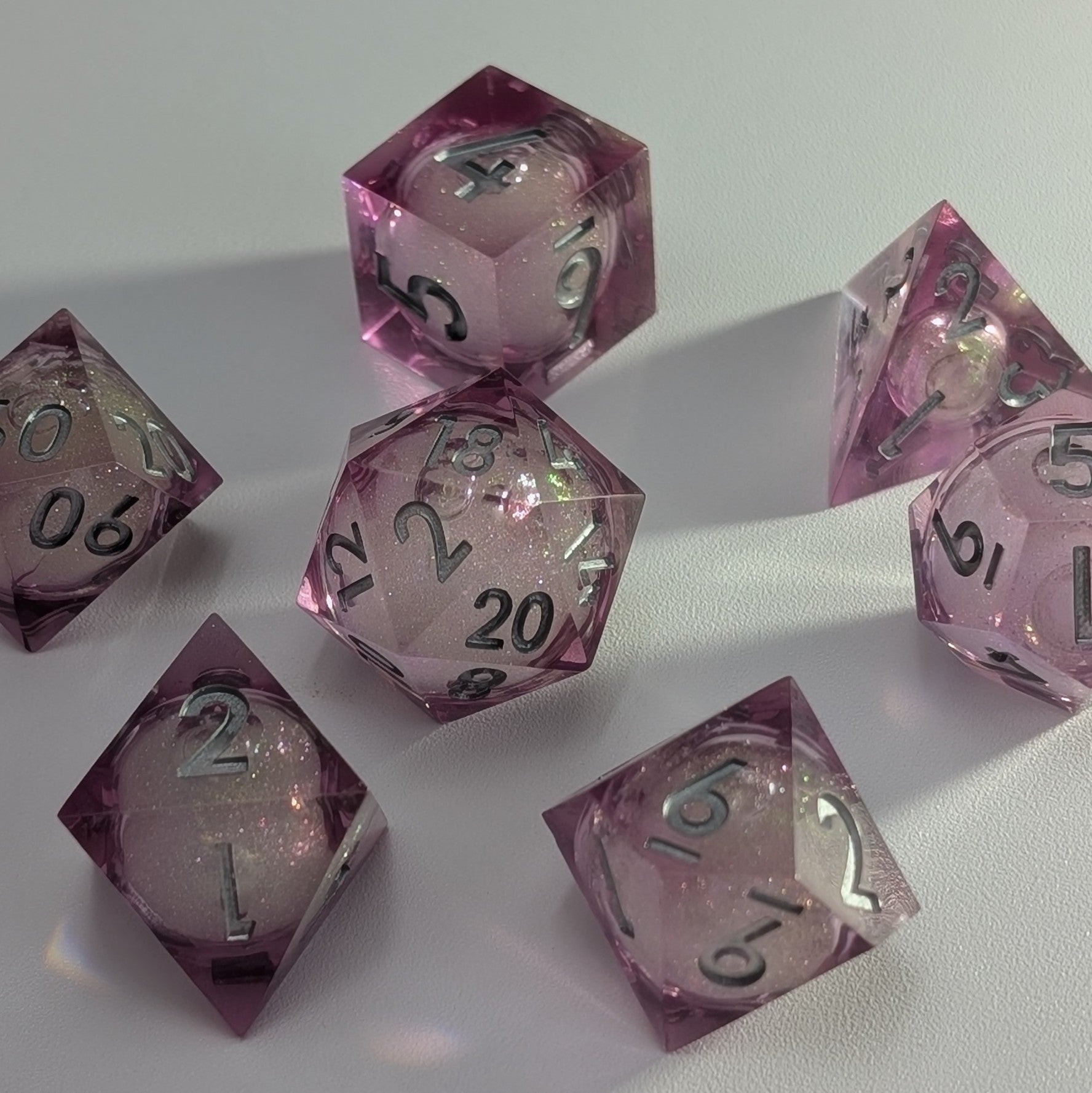 Sharp-edged pink DND dice set with a glittery liquid core and silver numbers, perfect for TTRPG sessions.