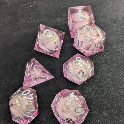 Handcrafted polyhedral dice set featuring translucent pink resin and a shimmering liquid center for roleplaying games on black background