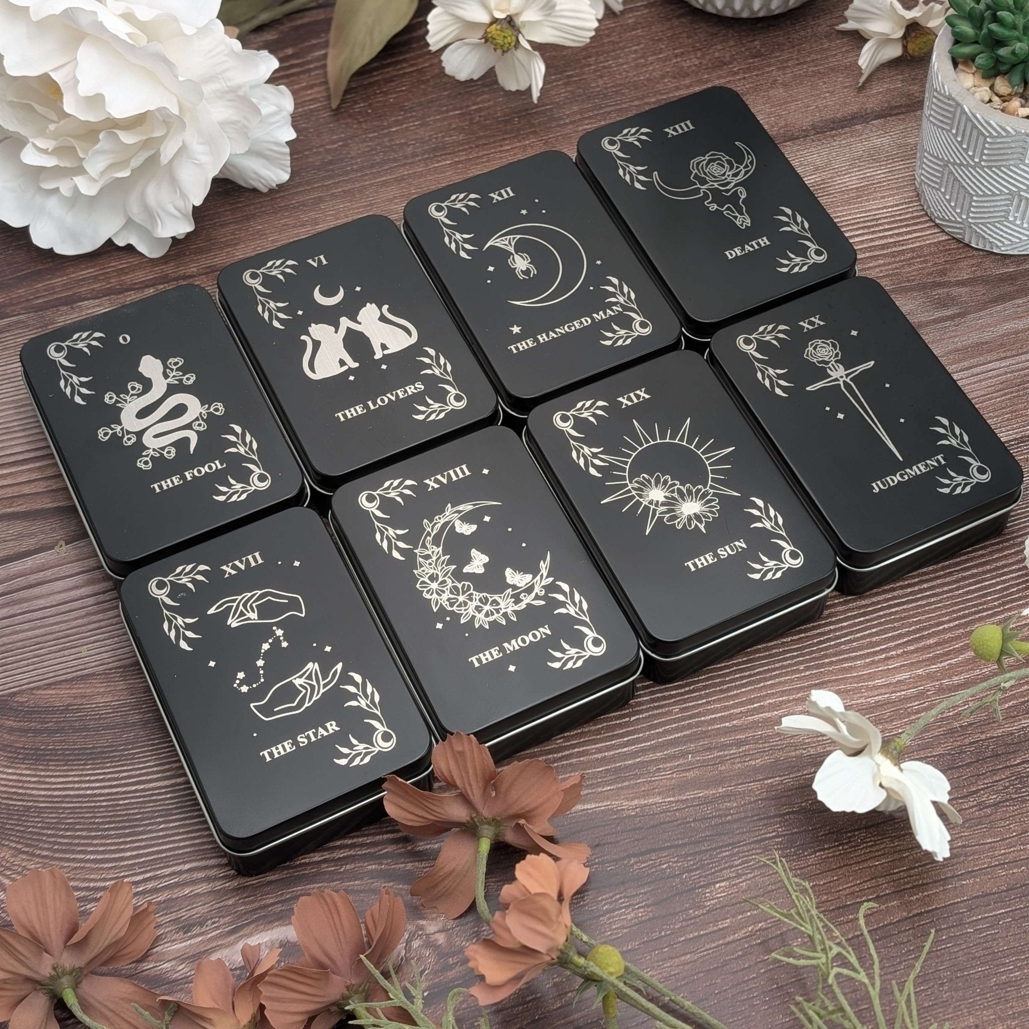 Photo of our tarot inspired dice tins for polyhedral dice storage on a woodgrain background with flowers
