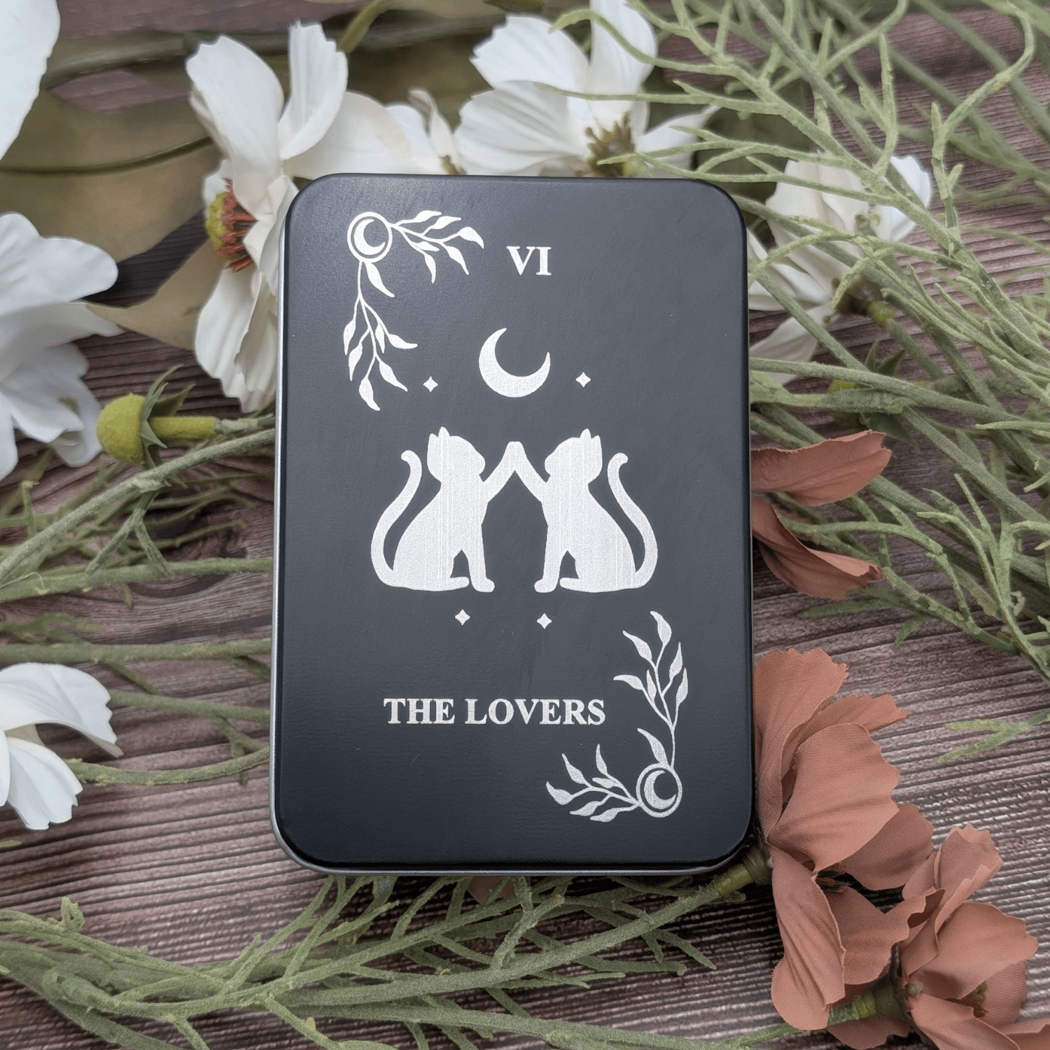 Engraved metal dice storage tin featuring a tarot inspired engraving called the lovers with two cats touching paws under a moon with celestial corners.