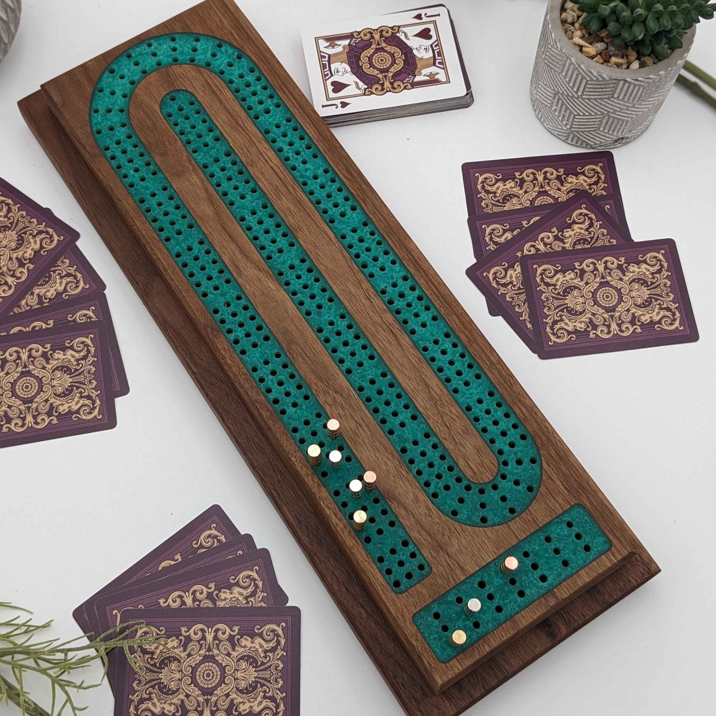 handmade walnut cribbage board with emerald epoxy resin inlay with card and page storage top view on white background and cards showing what it looks like playing