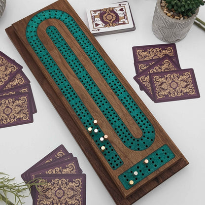 handmade walnut cribbage board with emerald epoxy resin inlay with card and page storage top view on white background and cards showing what it looks like playing