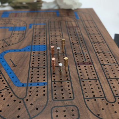 Close up shot of a walnut cribbage wars board with metal peg in the 3 lane board detailing the expoxy resin inlays with a natural bocca and white background.