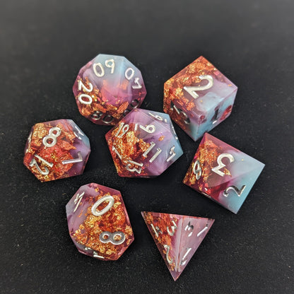 Blue and pink polyhedral dice with gold foil and silver inking on a black background